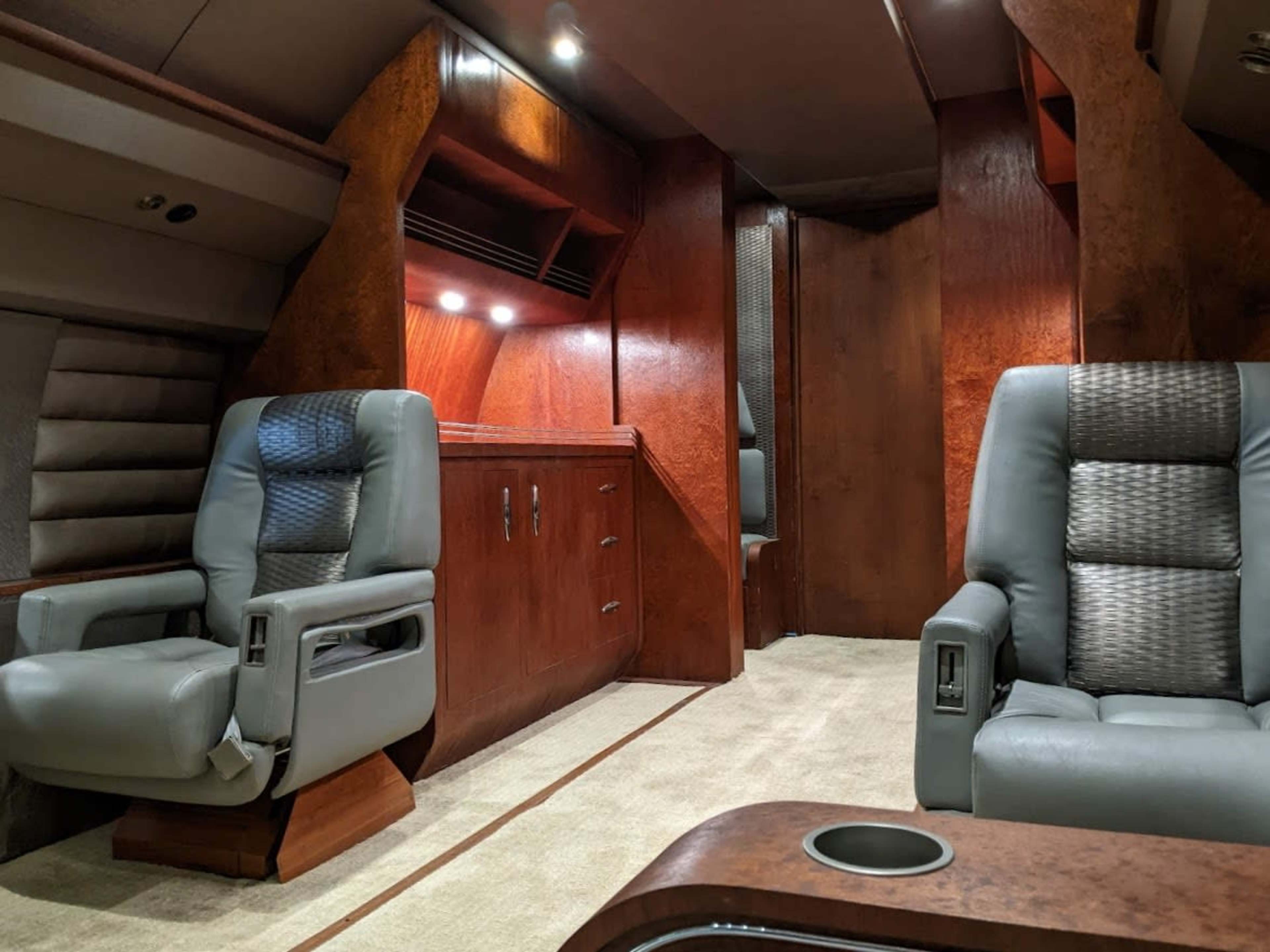 A spacious interior of a luxury lounge area with two leather chairs, wooden paneling, and a carpeted floor.