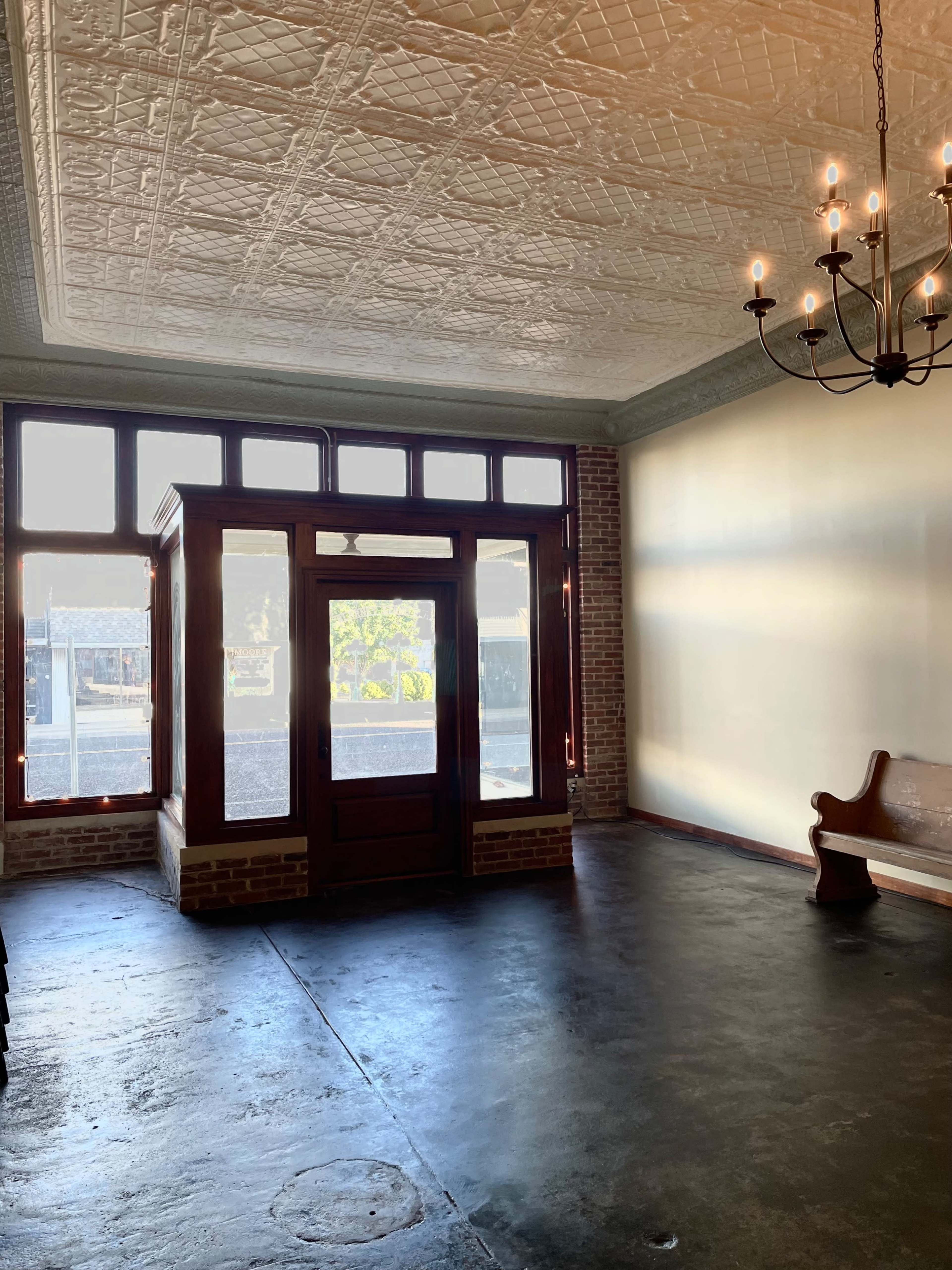 The interior features an empty room with a patterned ceiling, large windows, and a wooden bench against the wall.