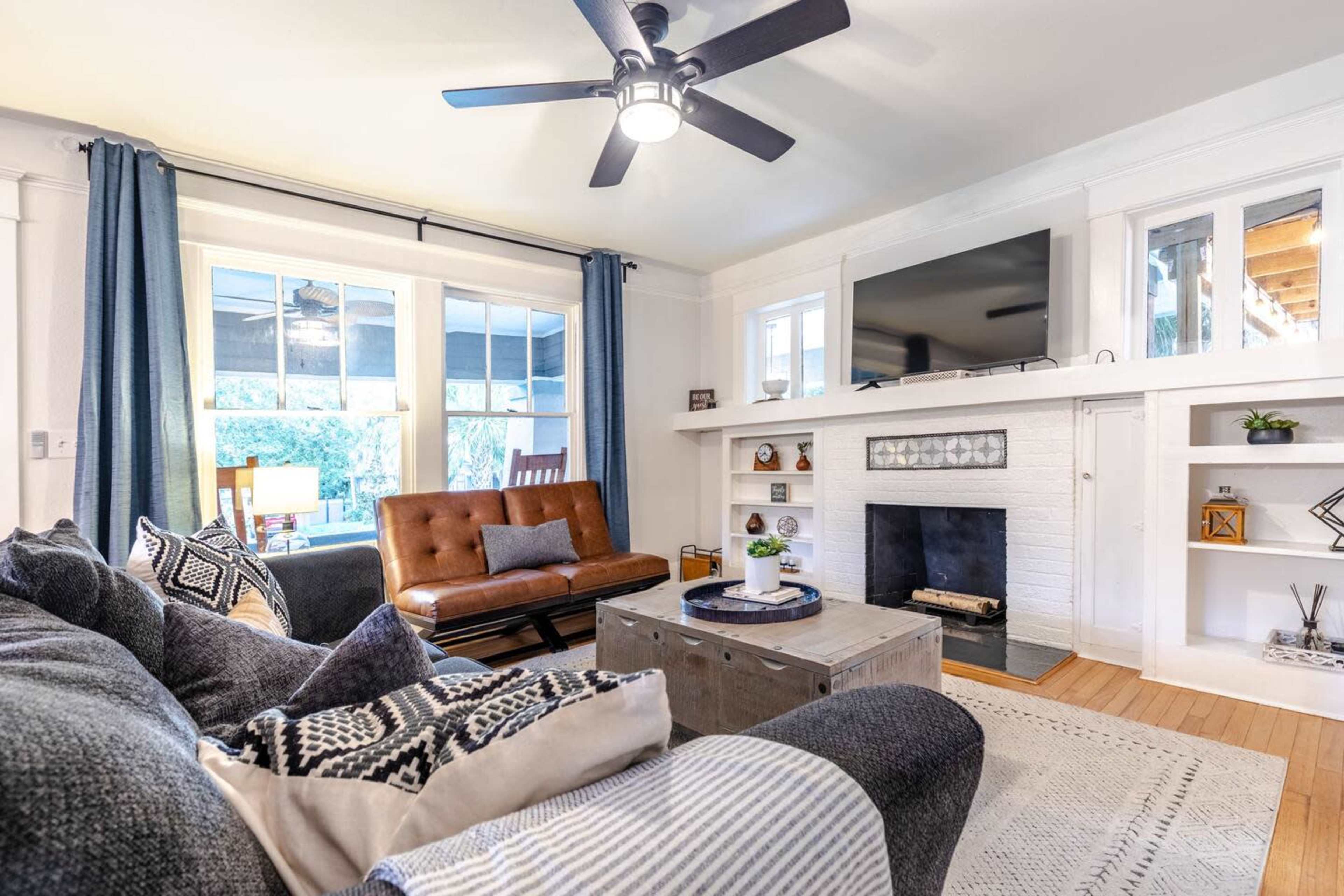 The image shows a cozy living room with a brown sofa, a coffee table, and a white mantelpiece, featuring a television above it and shelves filled with decorative items.