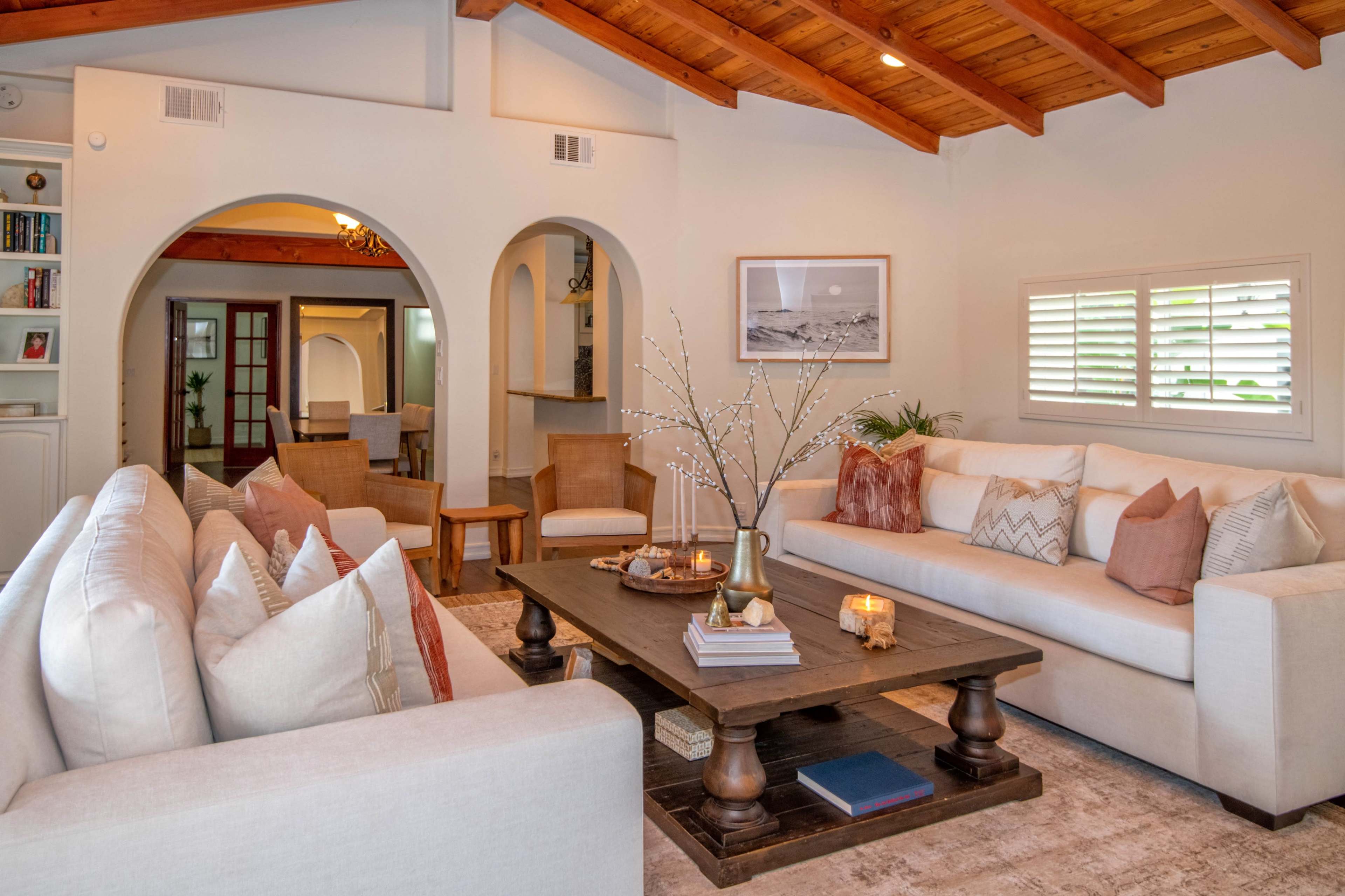 A spacious living room with high wooden ceilings, light-colored sofas, a central coffee table, and decorative elements.
