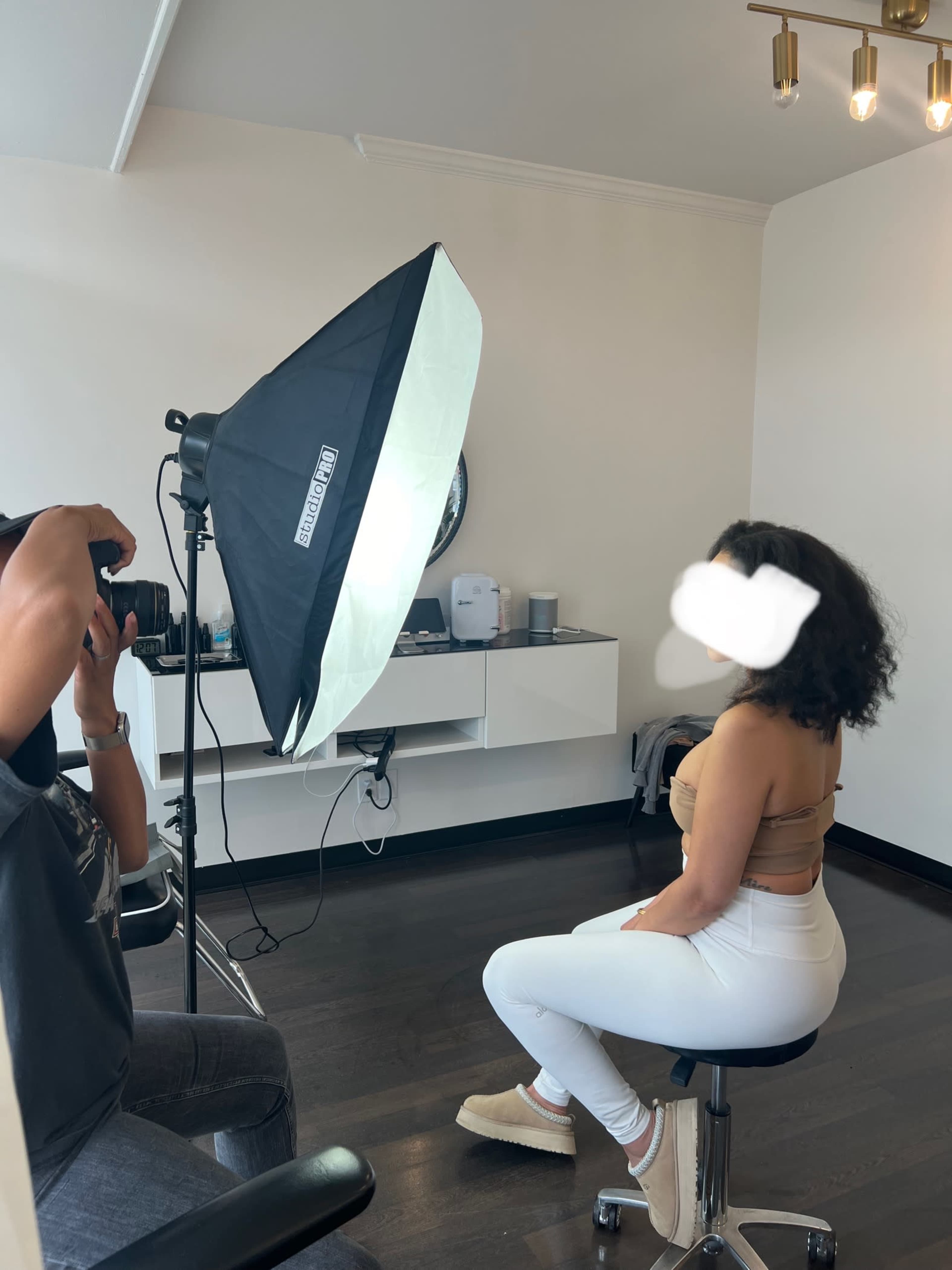 A photographer is capturing a seated model in a well-lit studio with a large softbox light.