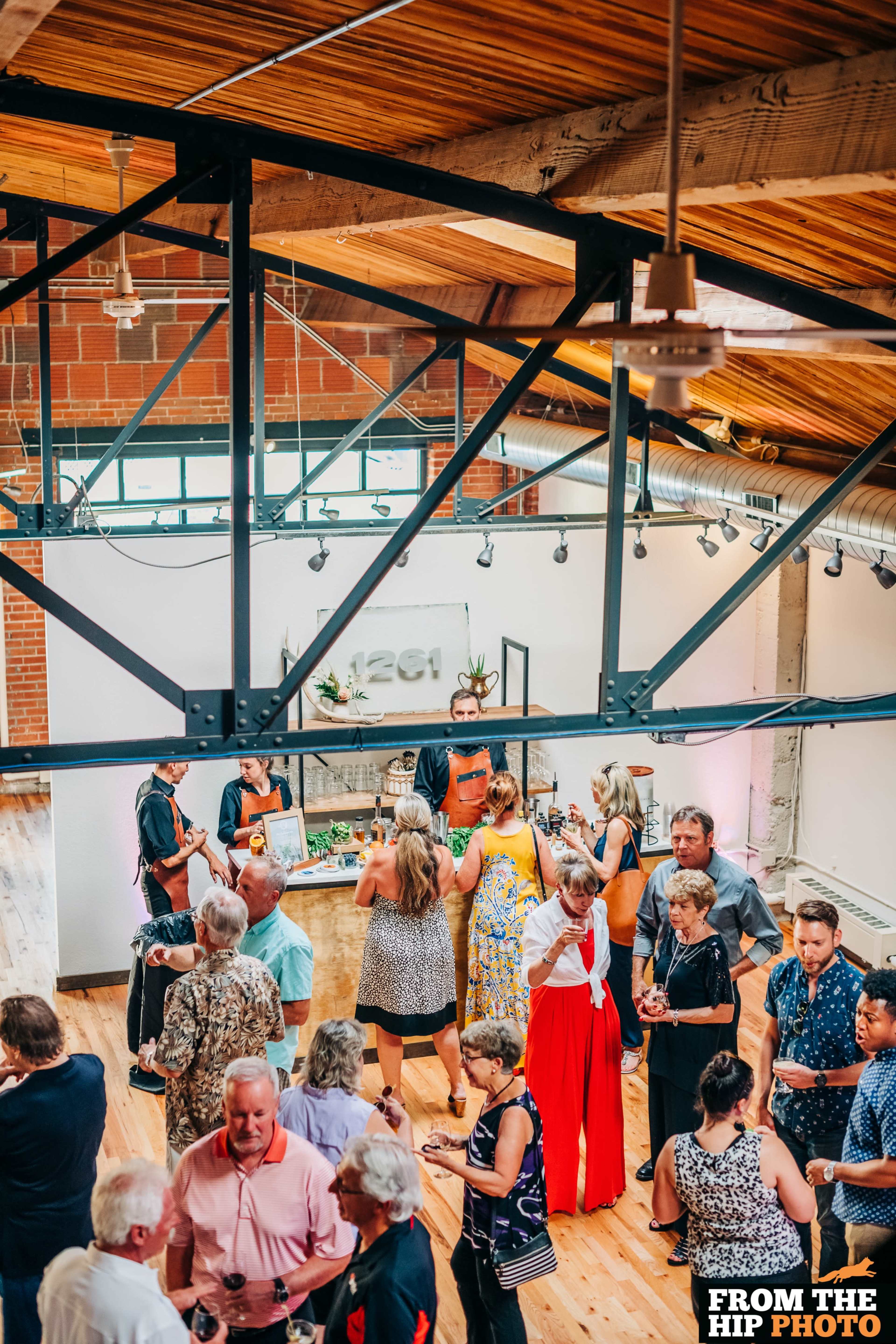A large group of people socialize at a modern event space featuring wooden beams and industrial design elements.