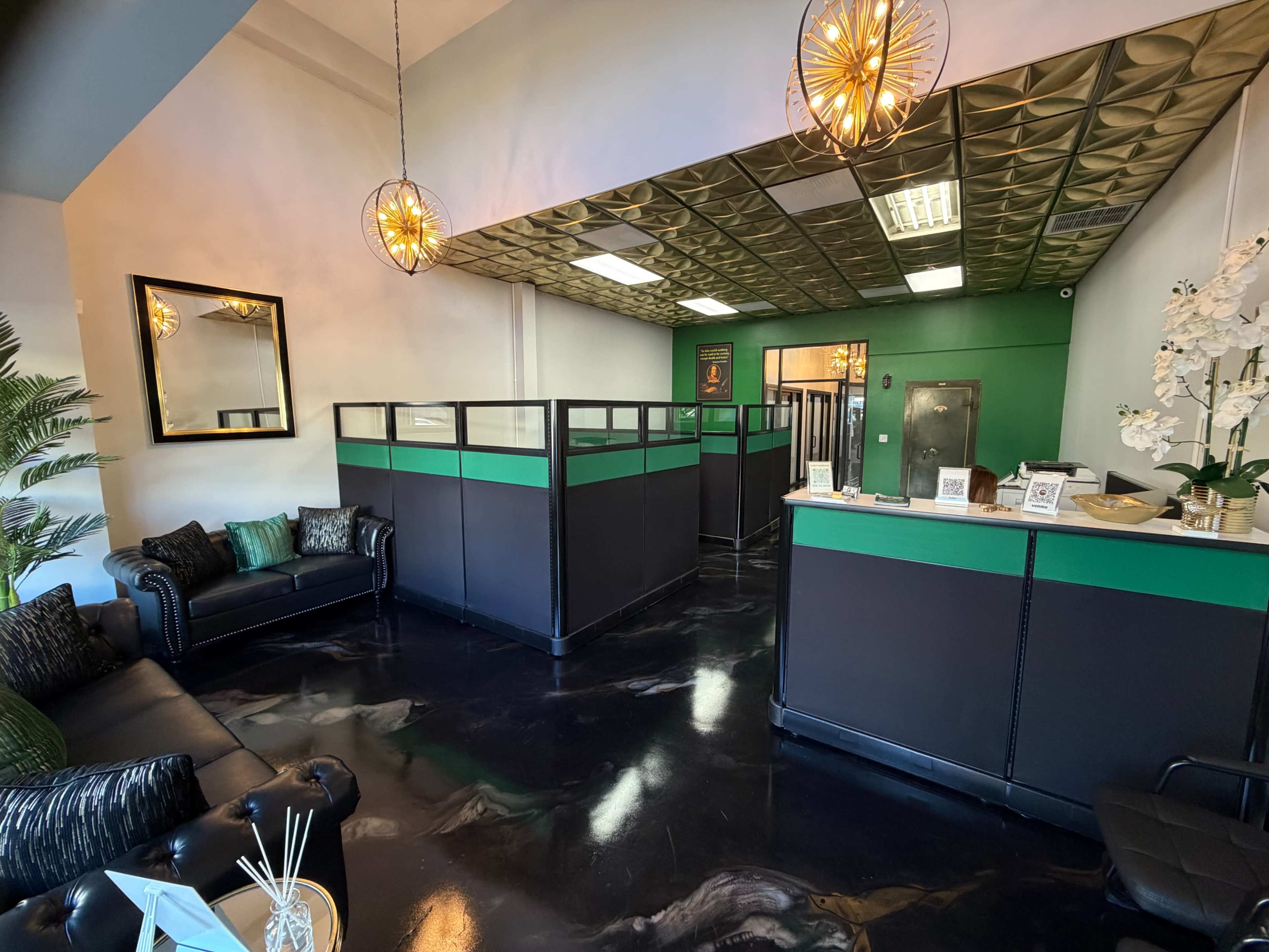 The image shows a modern reception area with black and green partitions, stylish lighting fixtures, and a sleek counter, surrounded by seating and decorative plants.