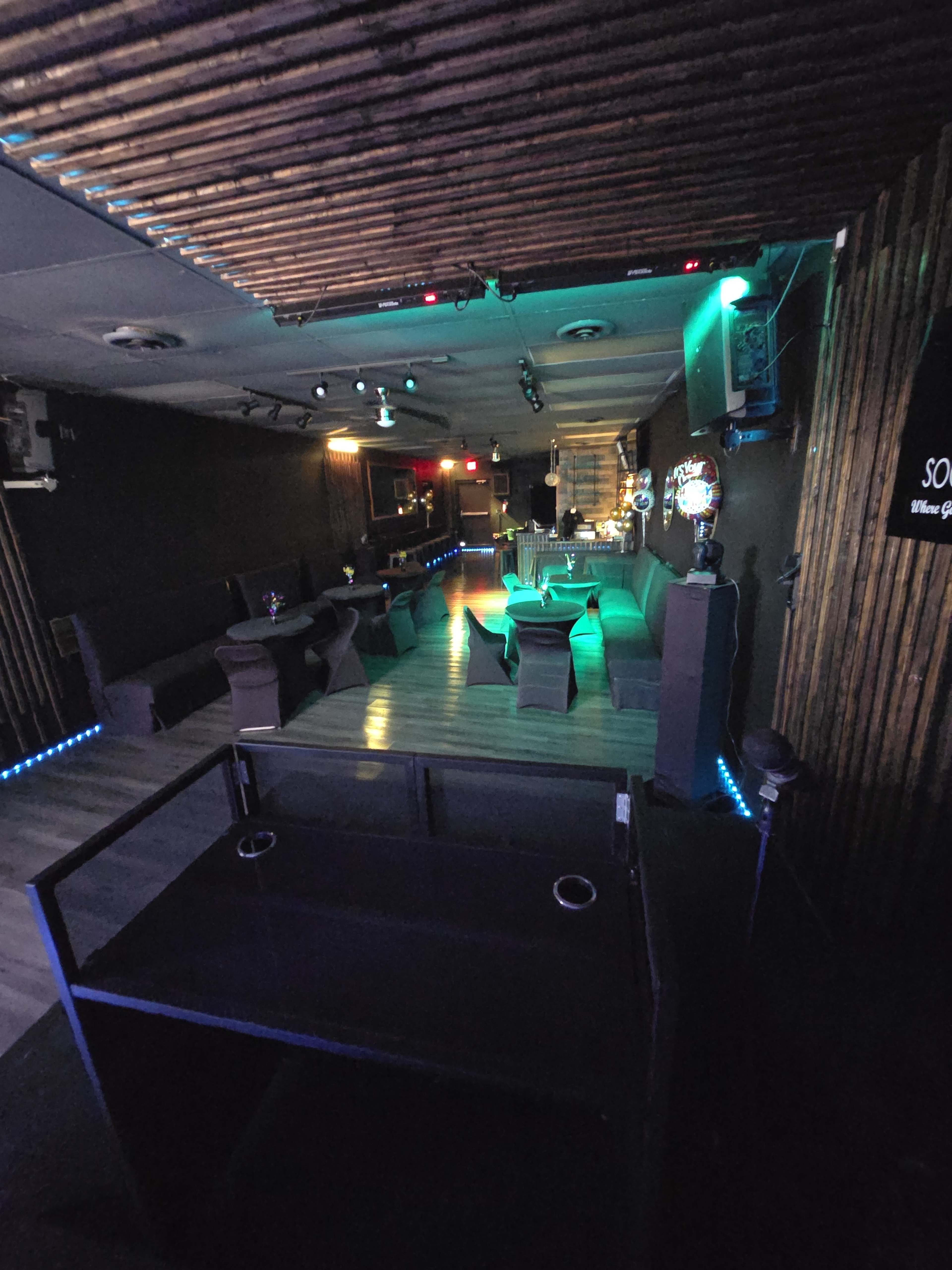 The image shows a dimly lit lounge with seating areas, a bar, and ambient lighting.