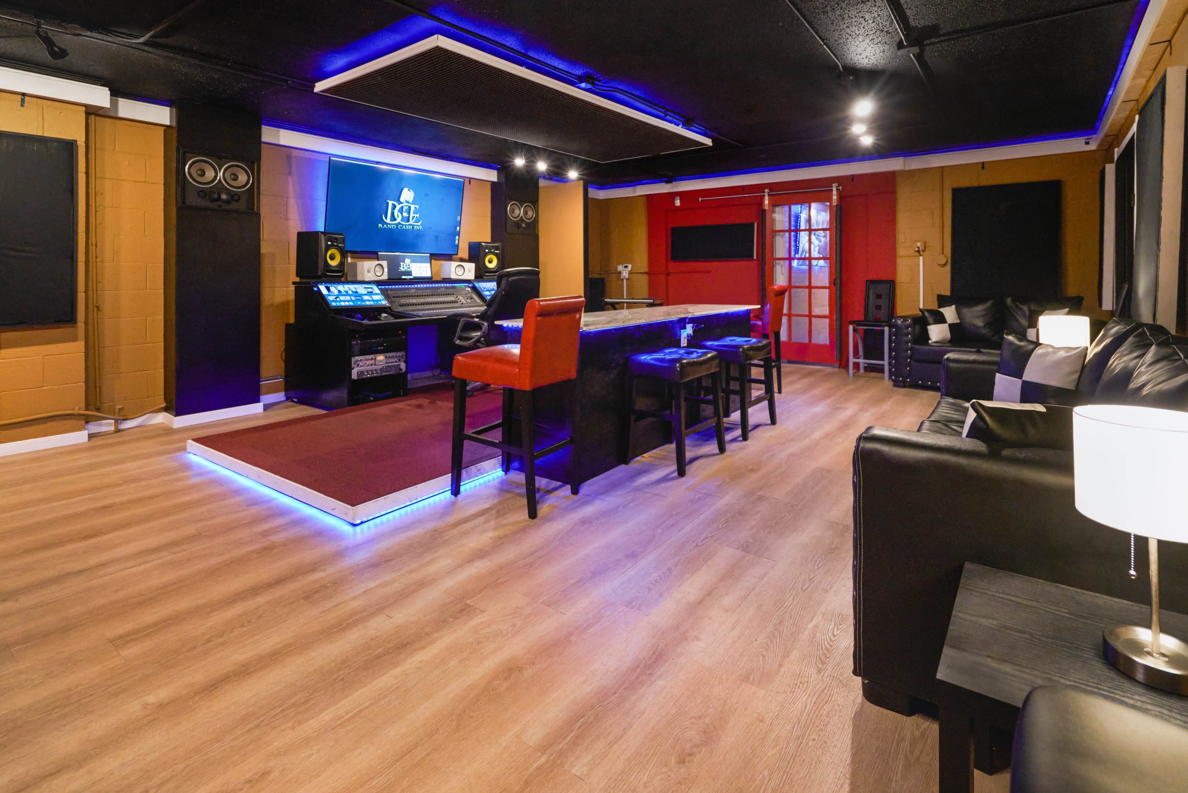 A modern recording studio featuring a central black bar with stools, a large screen on the wall, and comfortable seating areas.