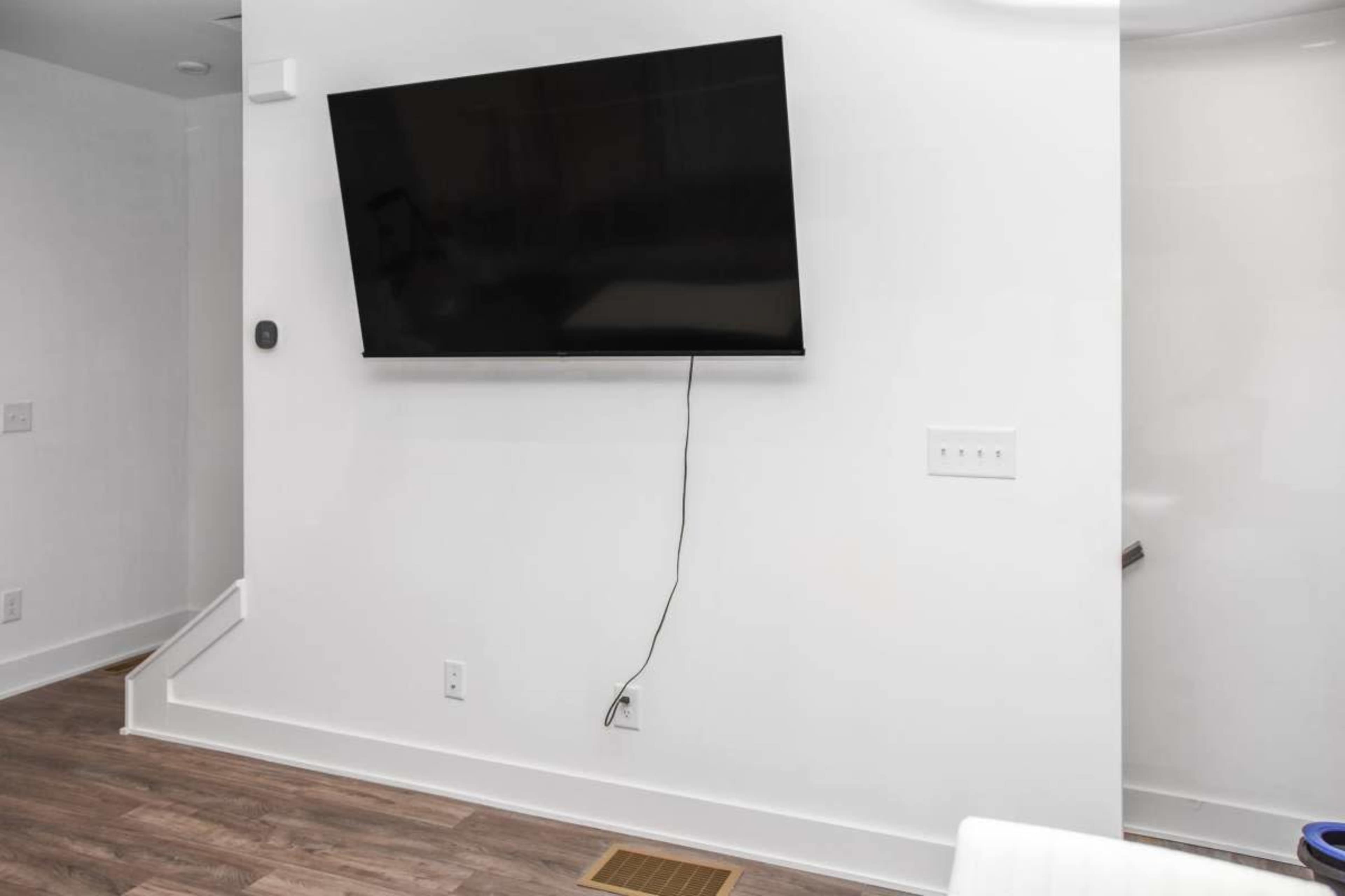 A flat-screen television is mounted on a white wall next to a stairway in a minimalist room.