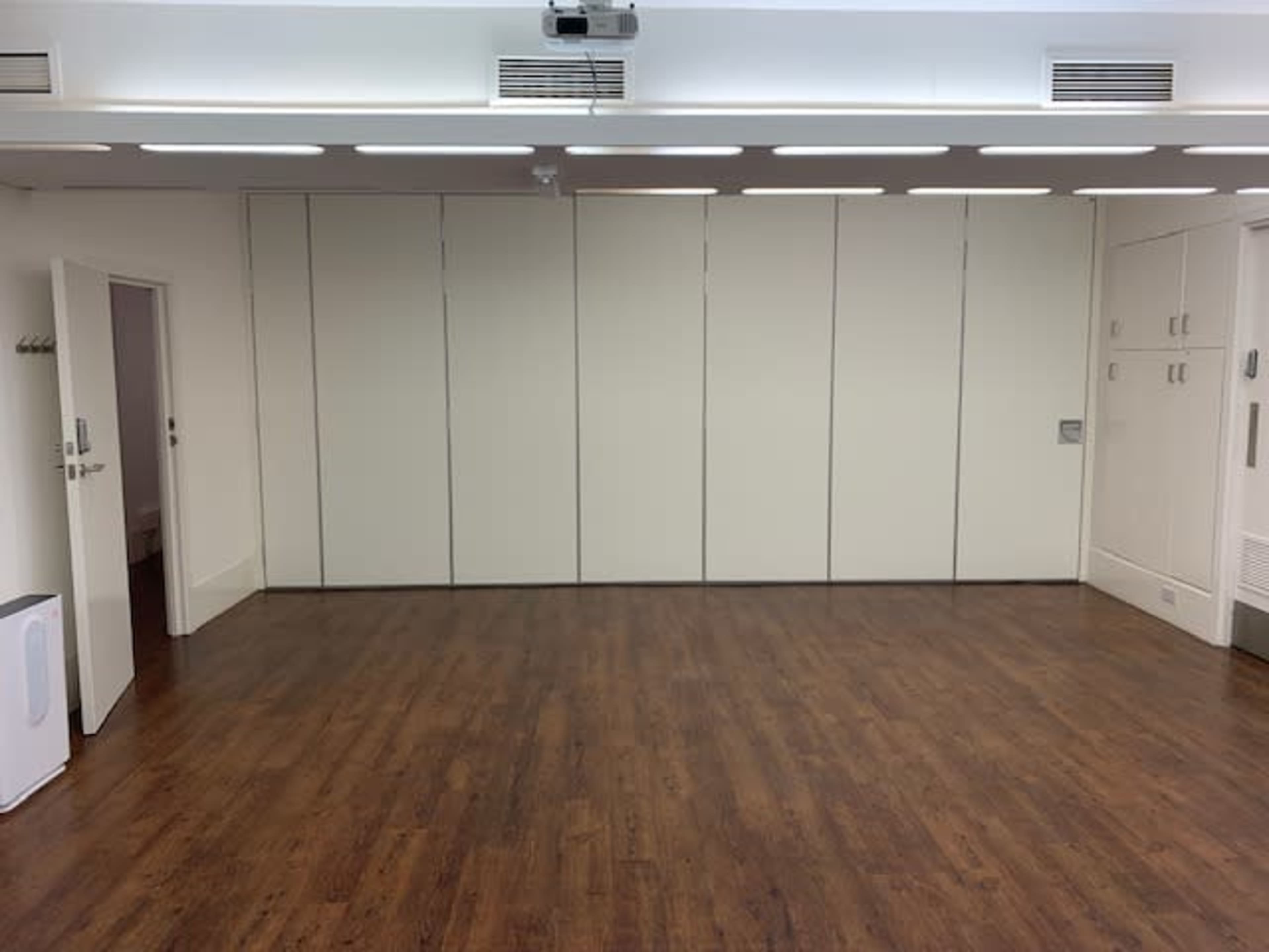 A spacious, empty room with hardwood flooring and white walls, featuring built-in cabinets and a door on one side.