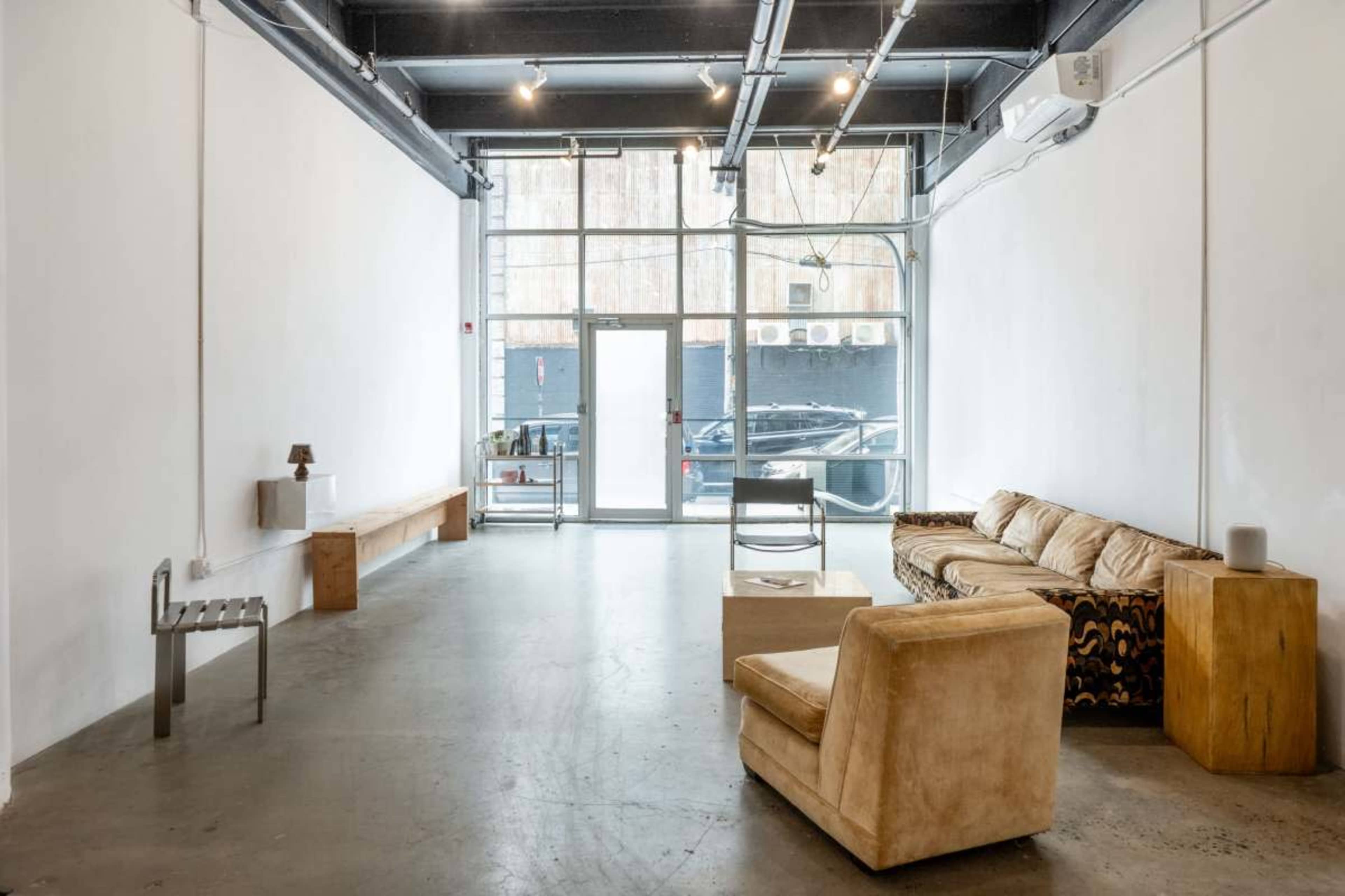 The image shows a spacious, minimalist interior with a simple seating arrangement, a coffee table, and large windows showcasing an entrance.