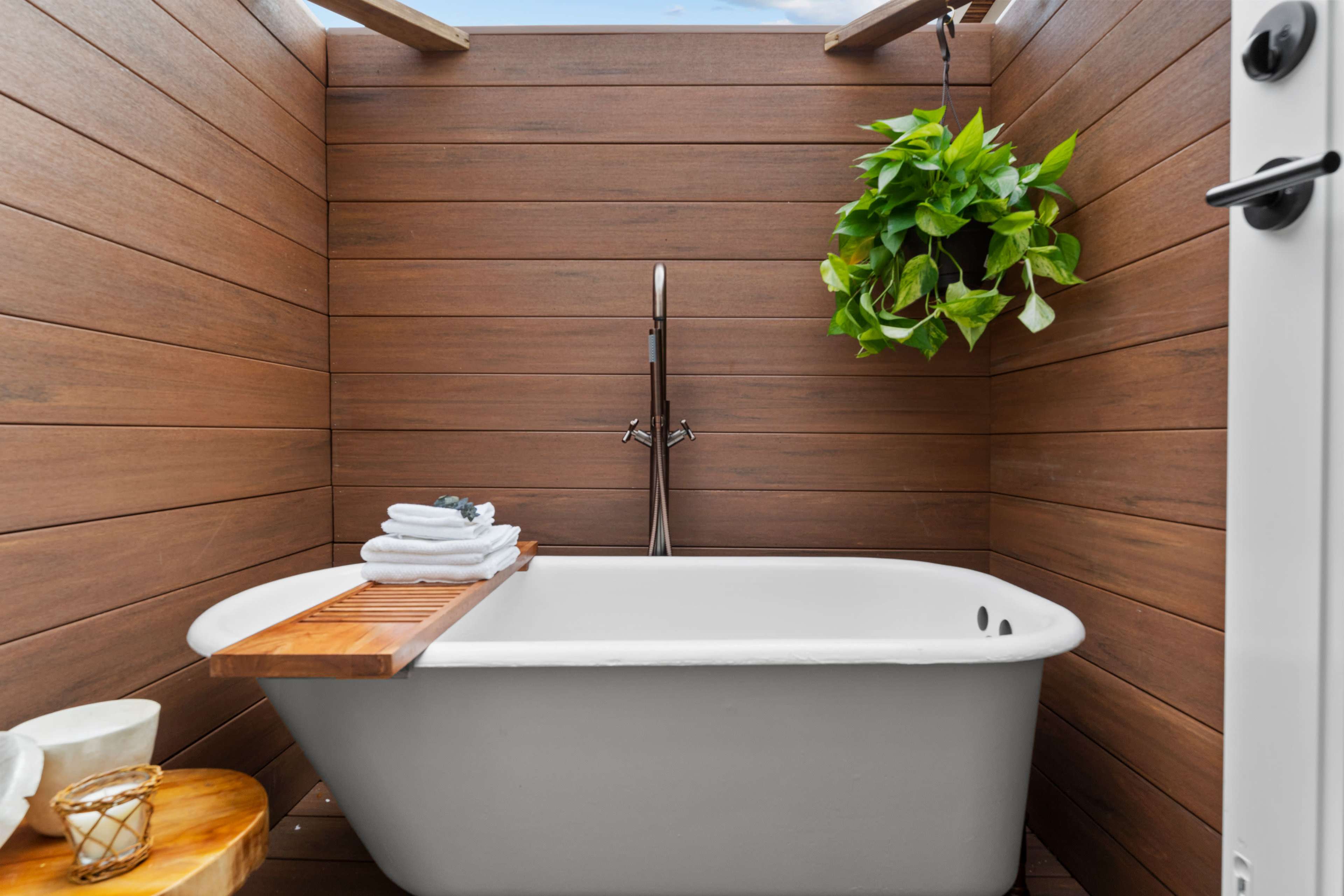 A modern, freestanding bathtub surrounded by wooden walls and a hanging plant.