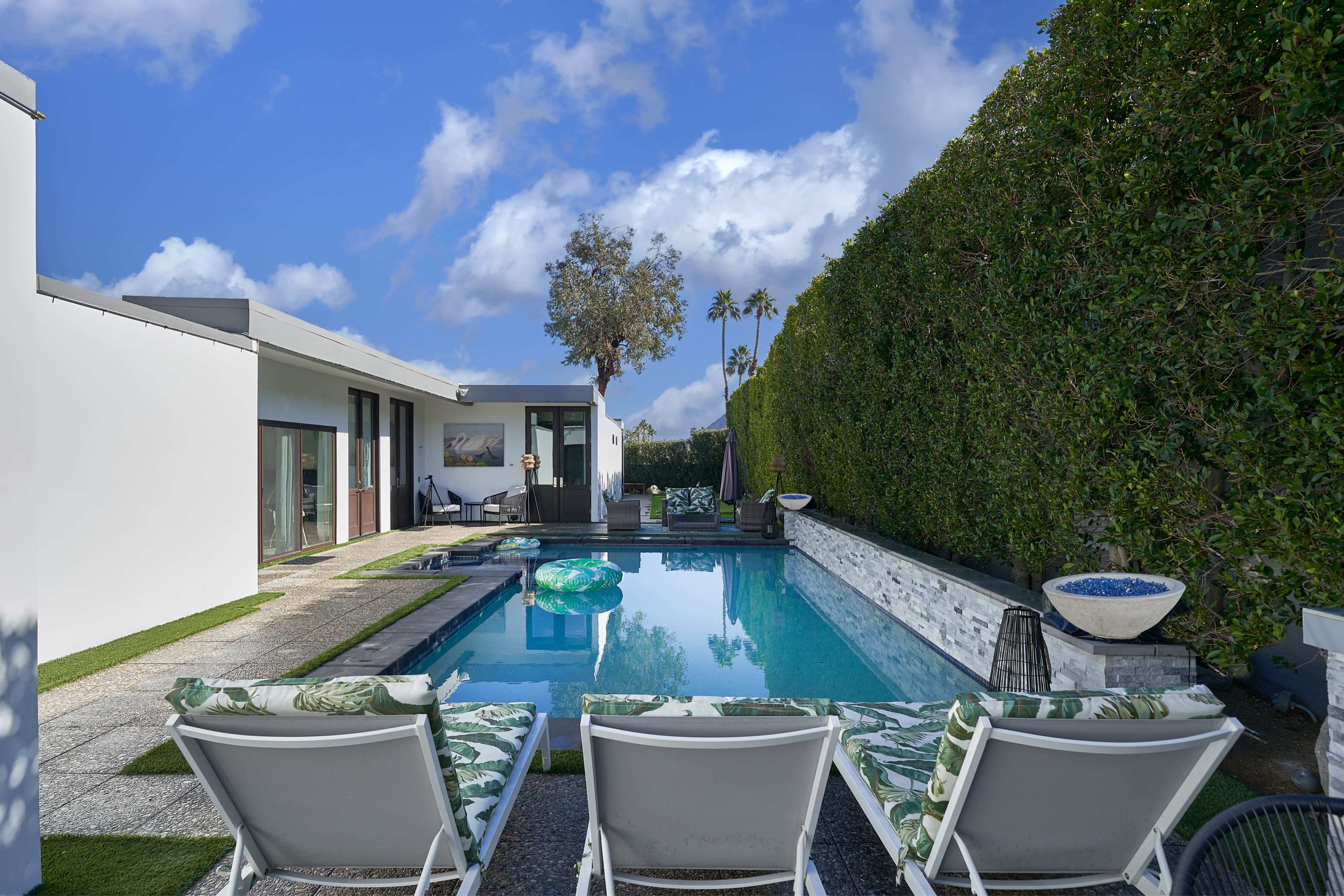 A modern backyard featuring a swimming pool with lounge chairs, surrounded by greenery and a sleek home in the background.