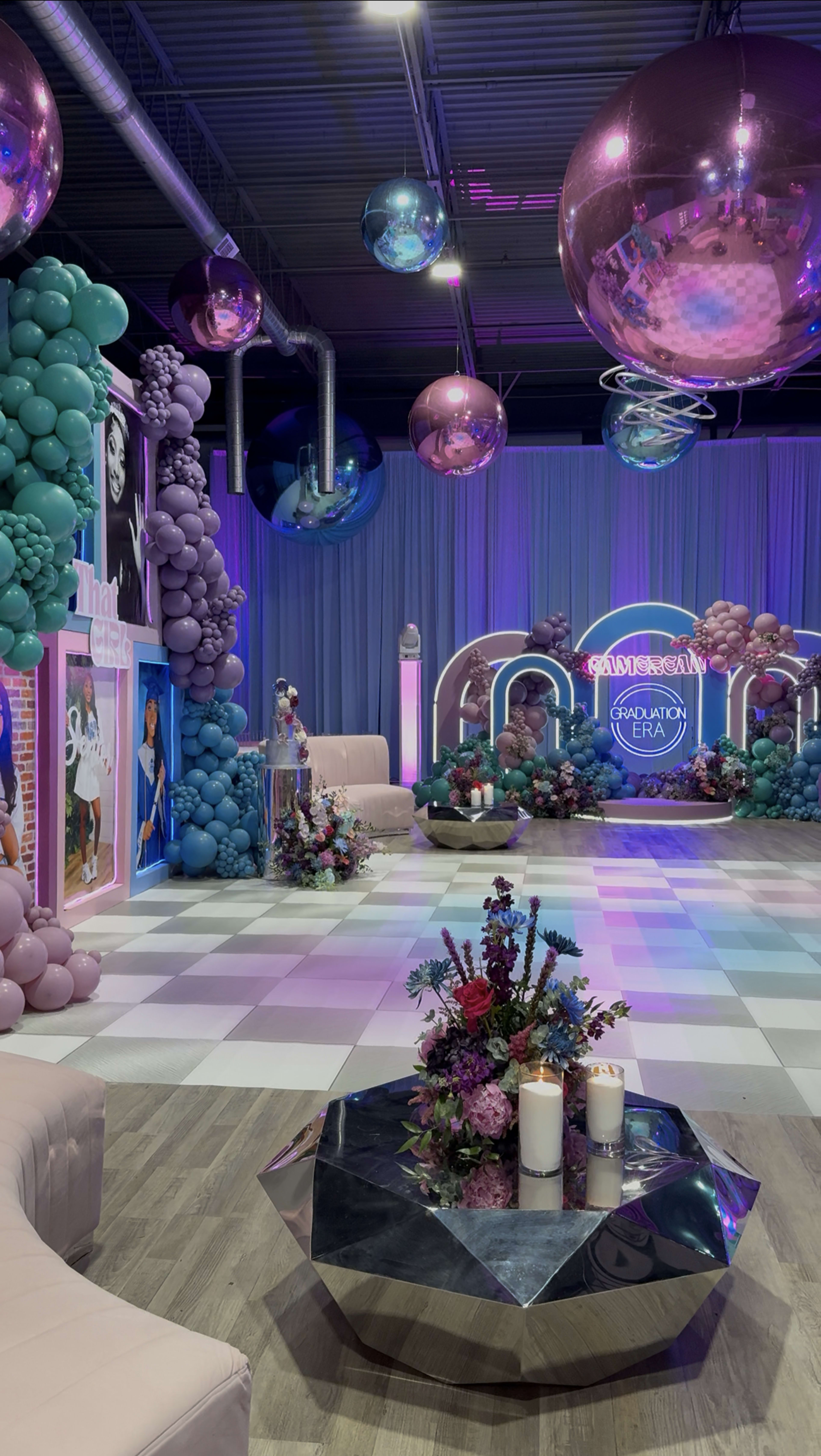 The image depicts a vibrant event space decorated with colorful balloons, floral arrangements, and ambient lighting, featuring a checkered floor and elegant seating.