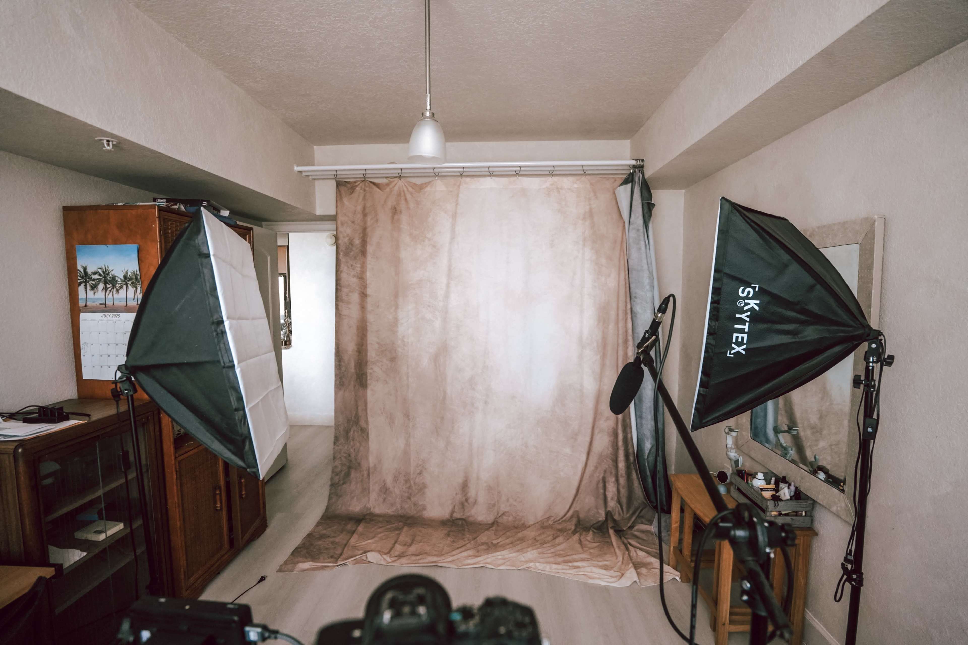 The image shows a photography studio setup with softbox lighting, a neutral backdrop, and a camera positioned on a tripod.