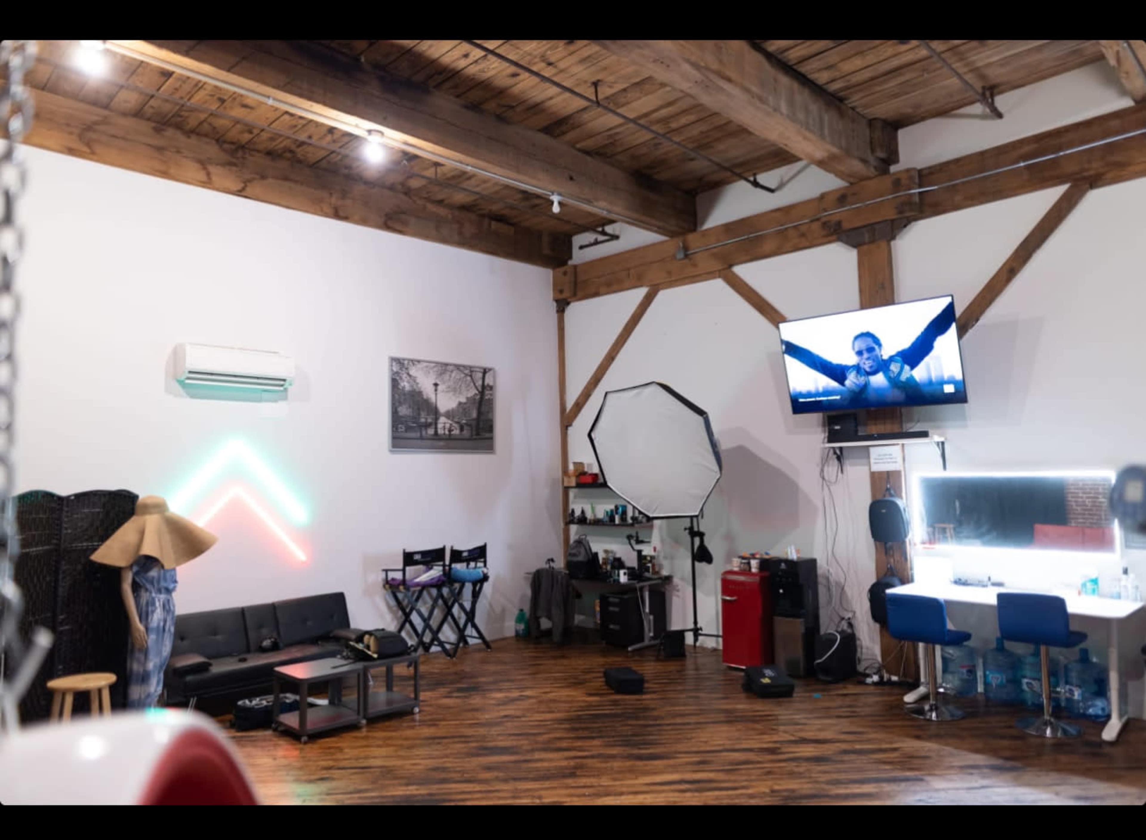 A stylistic photography studio with wooden beams, a couch, a makeup station, and a large monitor displaying an image on the wall.