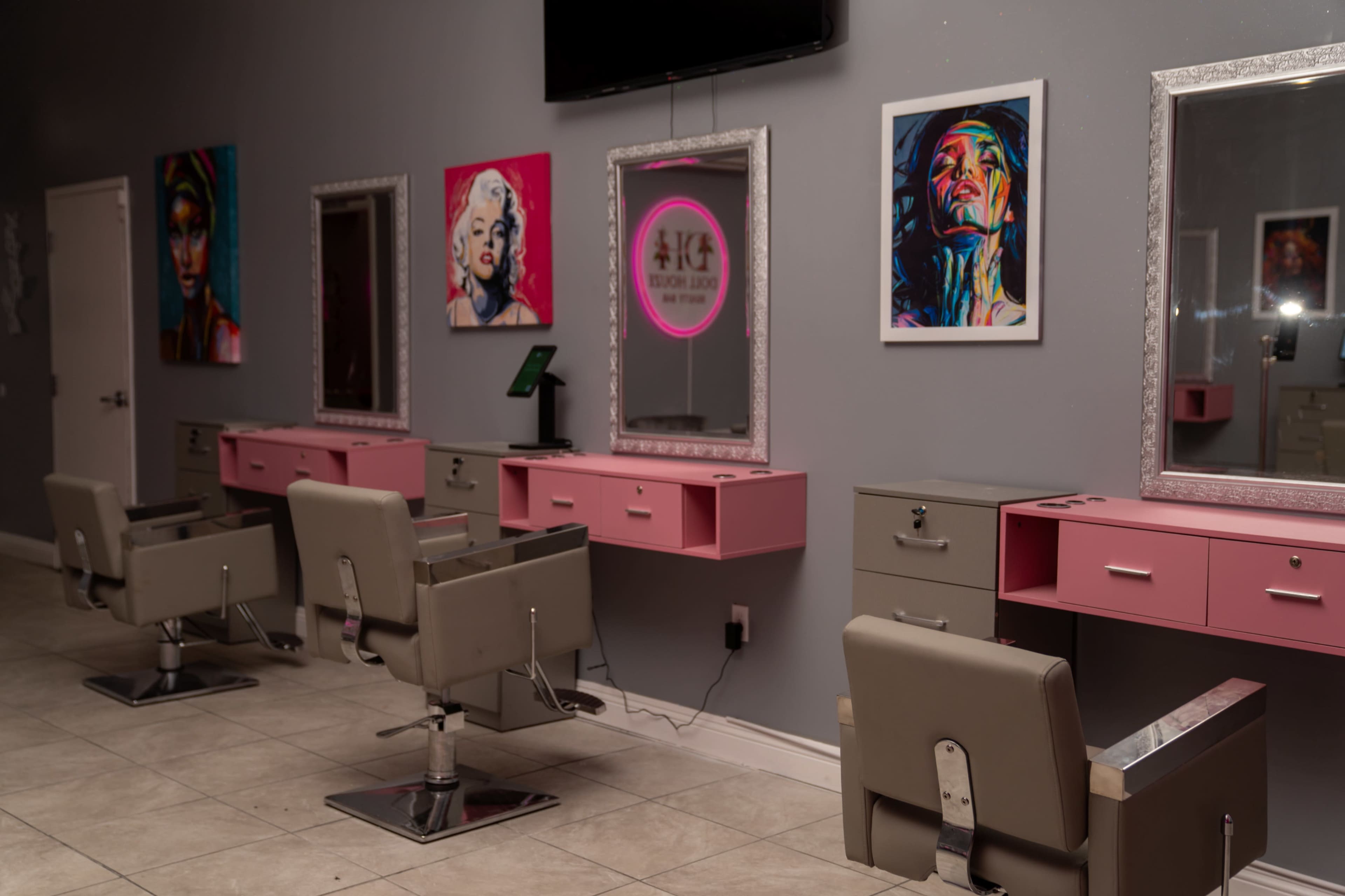 A modern salon interior with four styling stations, each equipped with a chair and a mirror, adorned with colorful artwork on the walls.