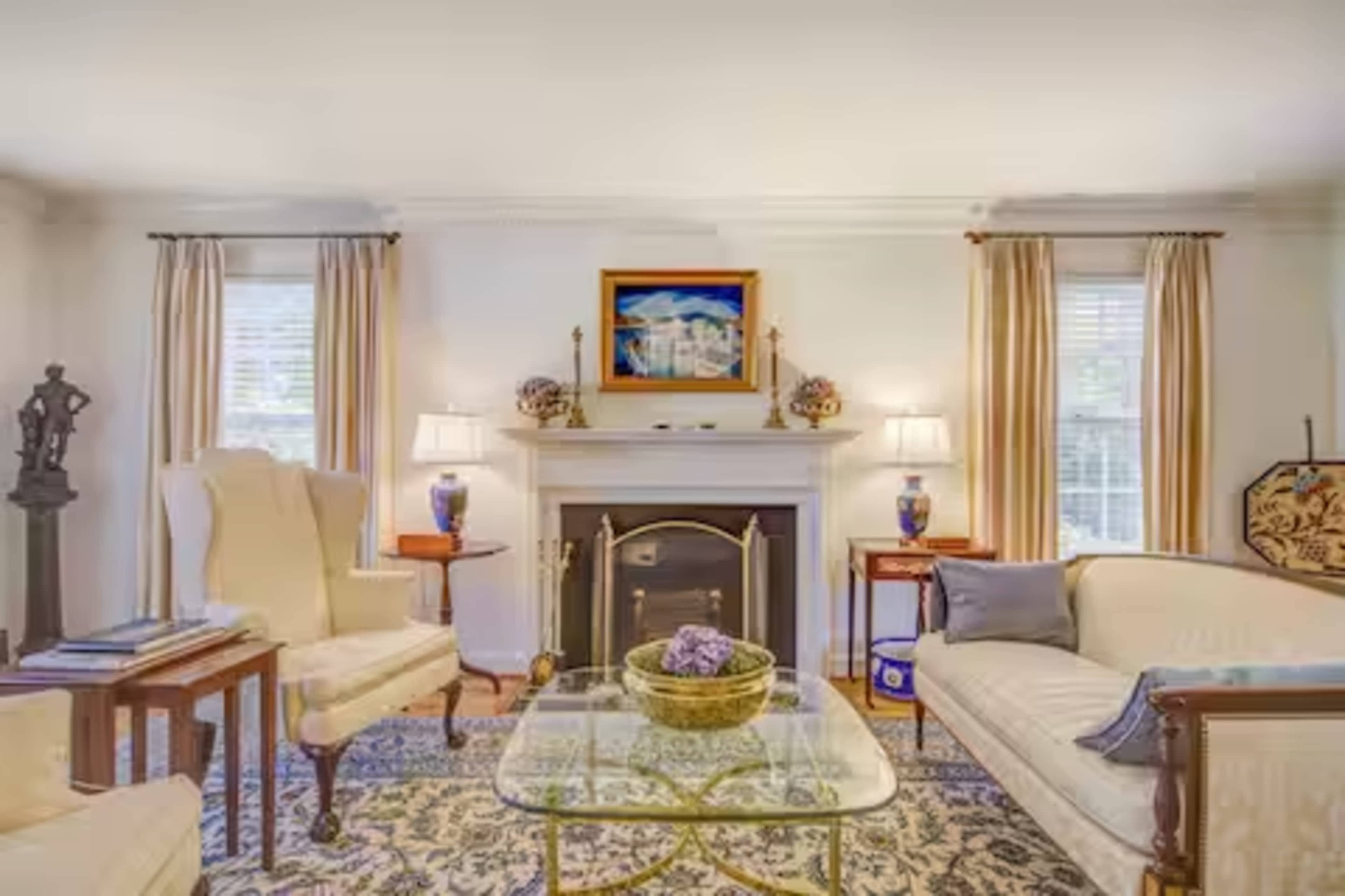 The living room features two armchairs and a sofa arranged around a glass coffee table, with a fireplace and artwork displayed above it.