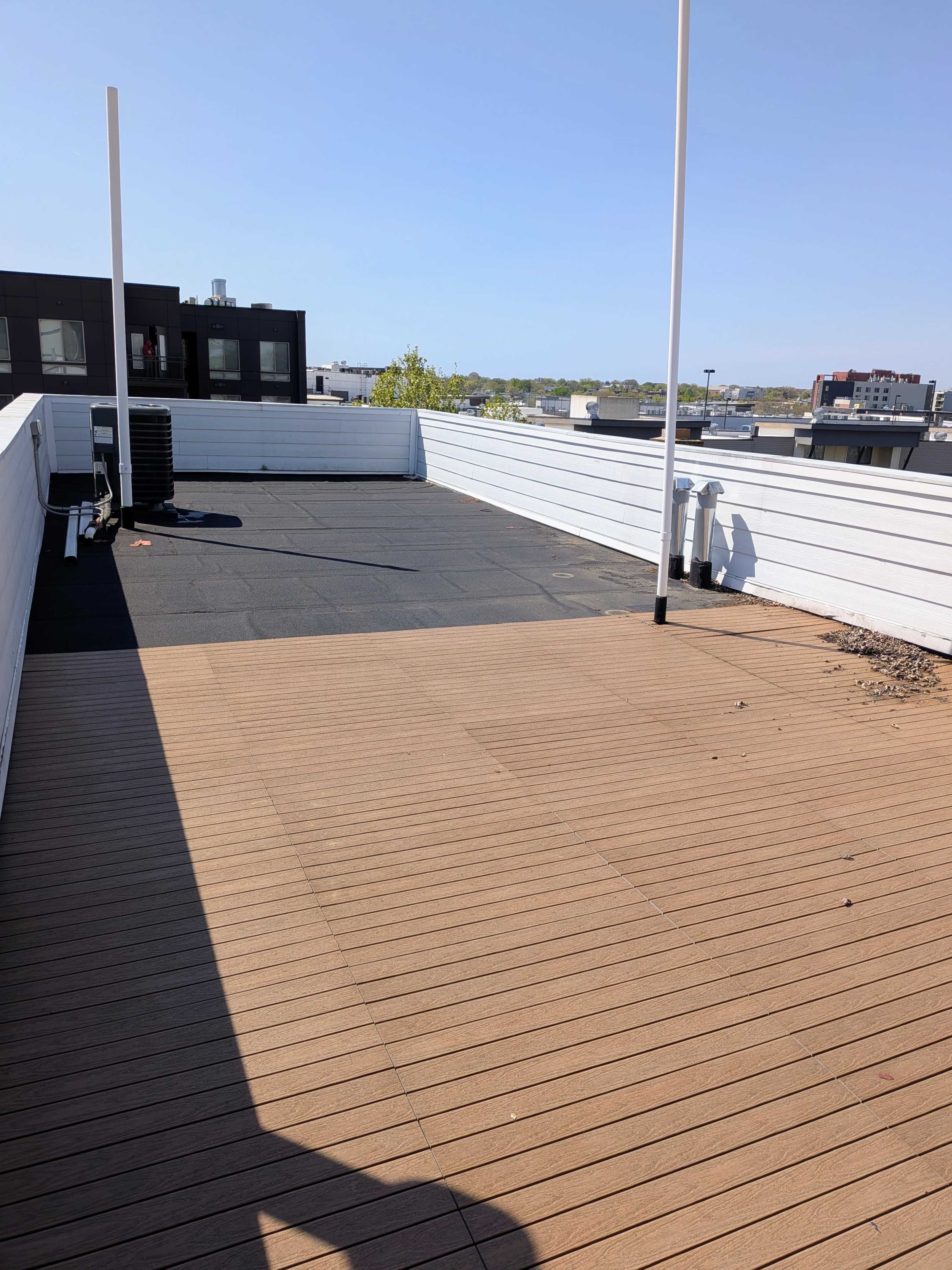 The image shows a flat rooftop terrace with sections of wooden and black surfaces under clear blue skies.