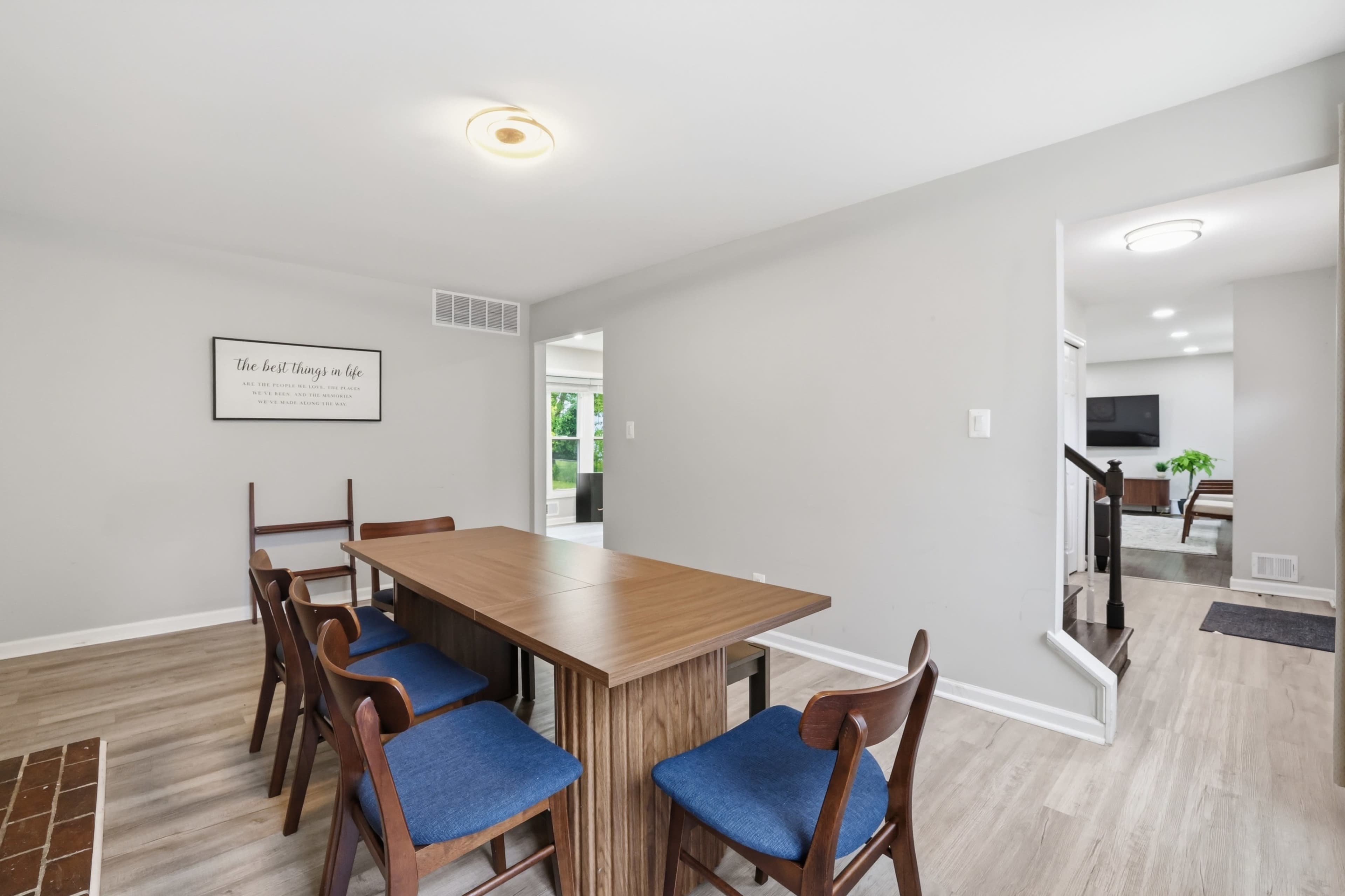 A modern dining area features a wooden table surrounded by chairs, with a wall-mounted sign and an open passage leading to another room.