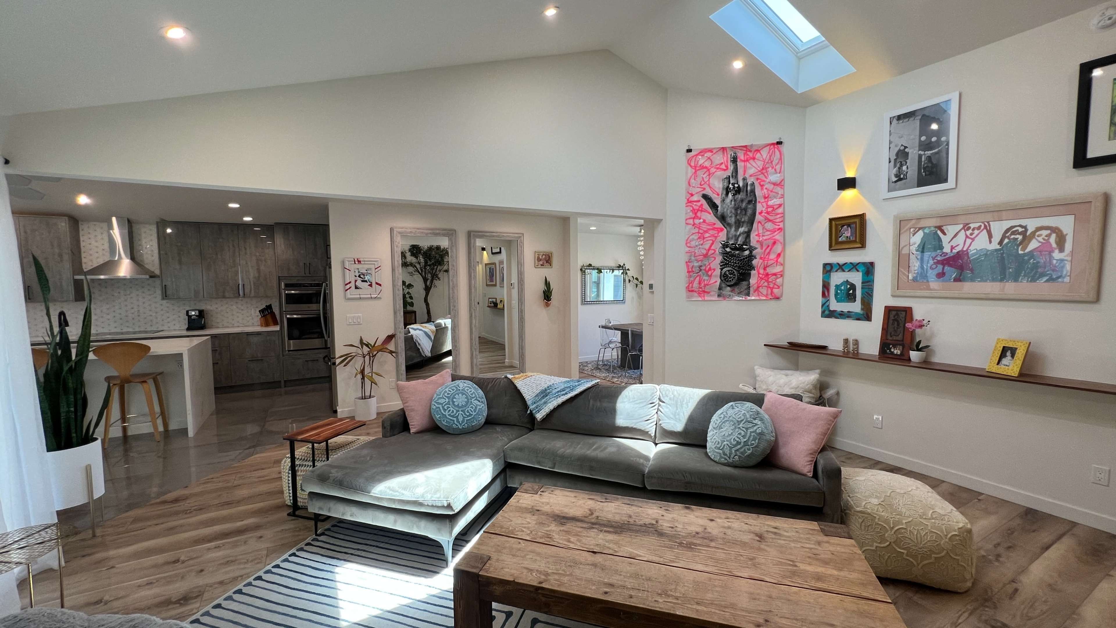 A modern living room with a sectional sofa, wooden coffee table, and walls adorned with artwork, leading into an open kitchen in the background.