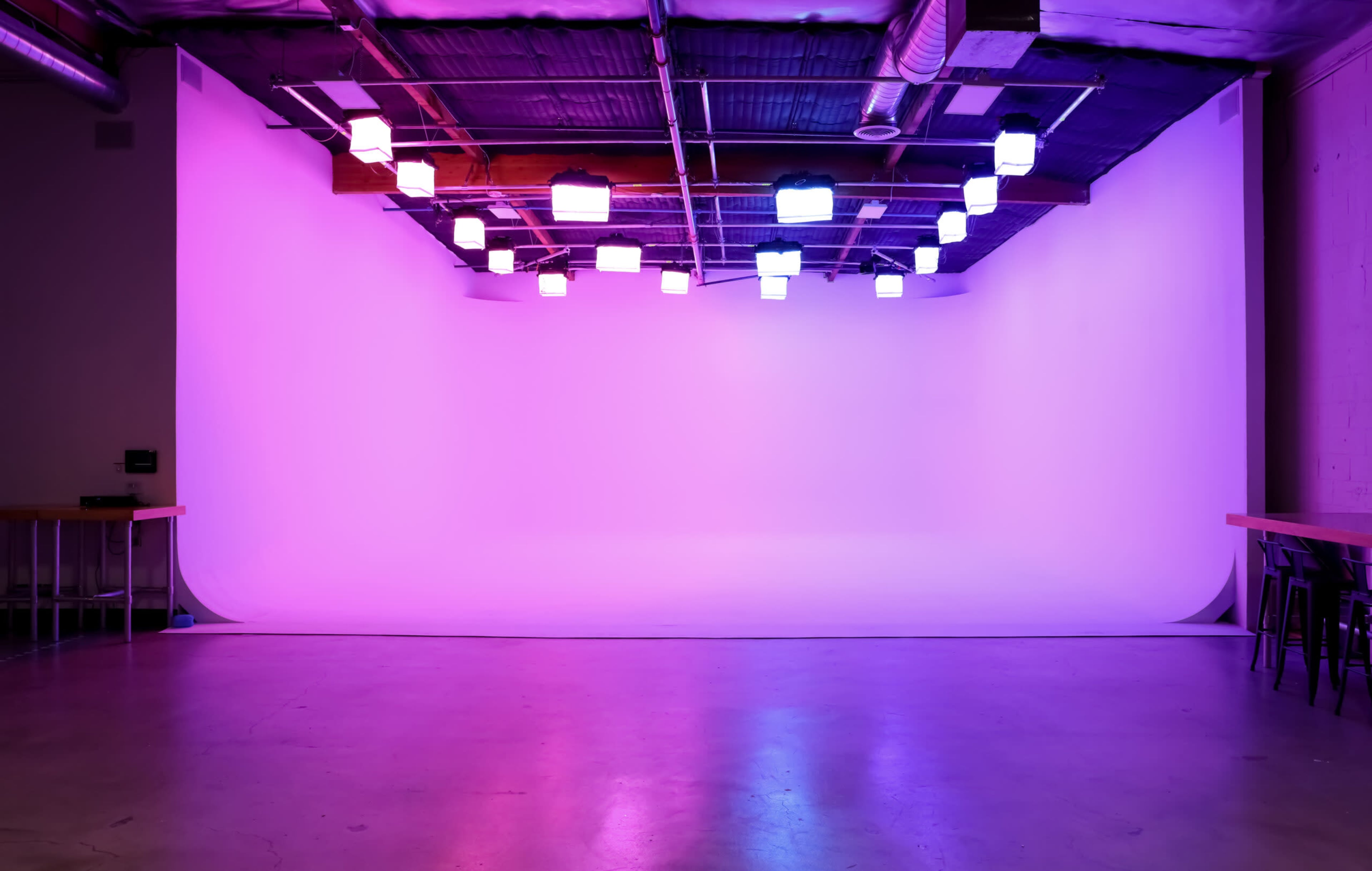 A studio space features a blank backdrop illuminated by colorful overhead lights.