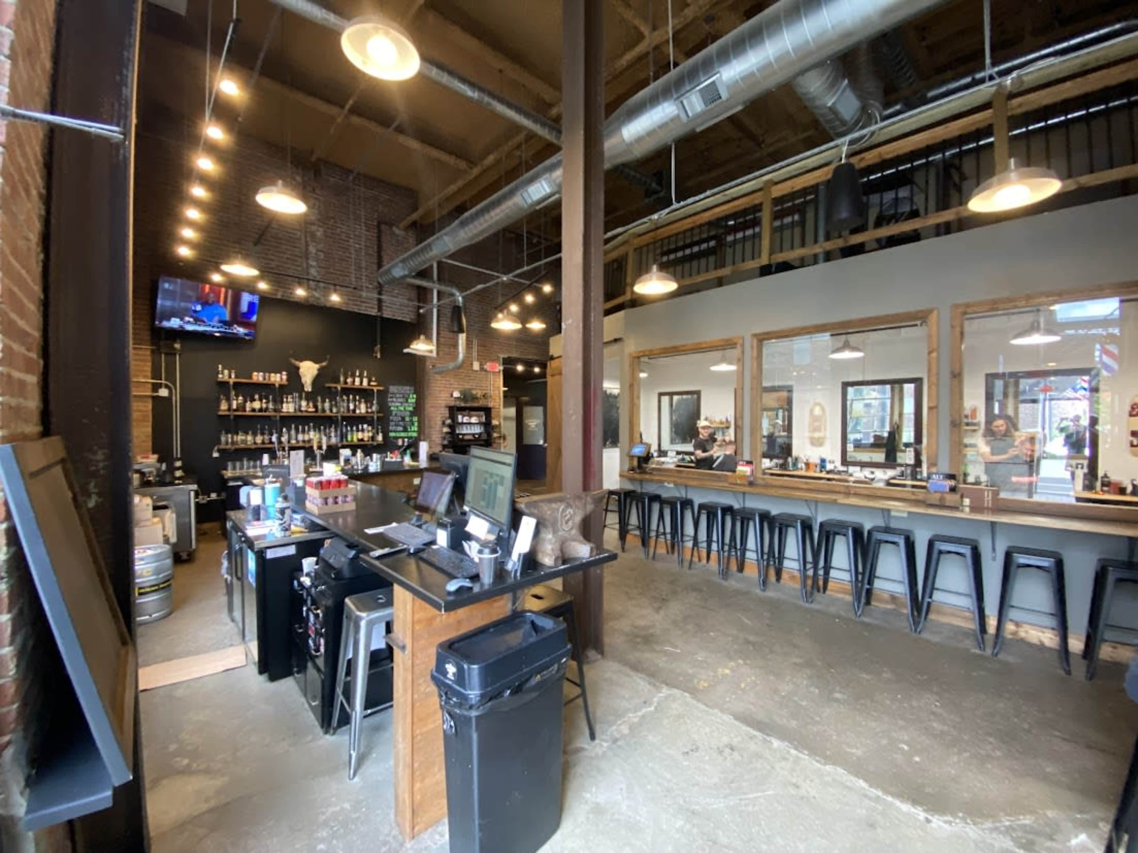The image shows the interior of a barbershop with a waiting area and a service counter featuring hair grooming products.