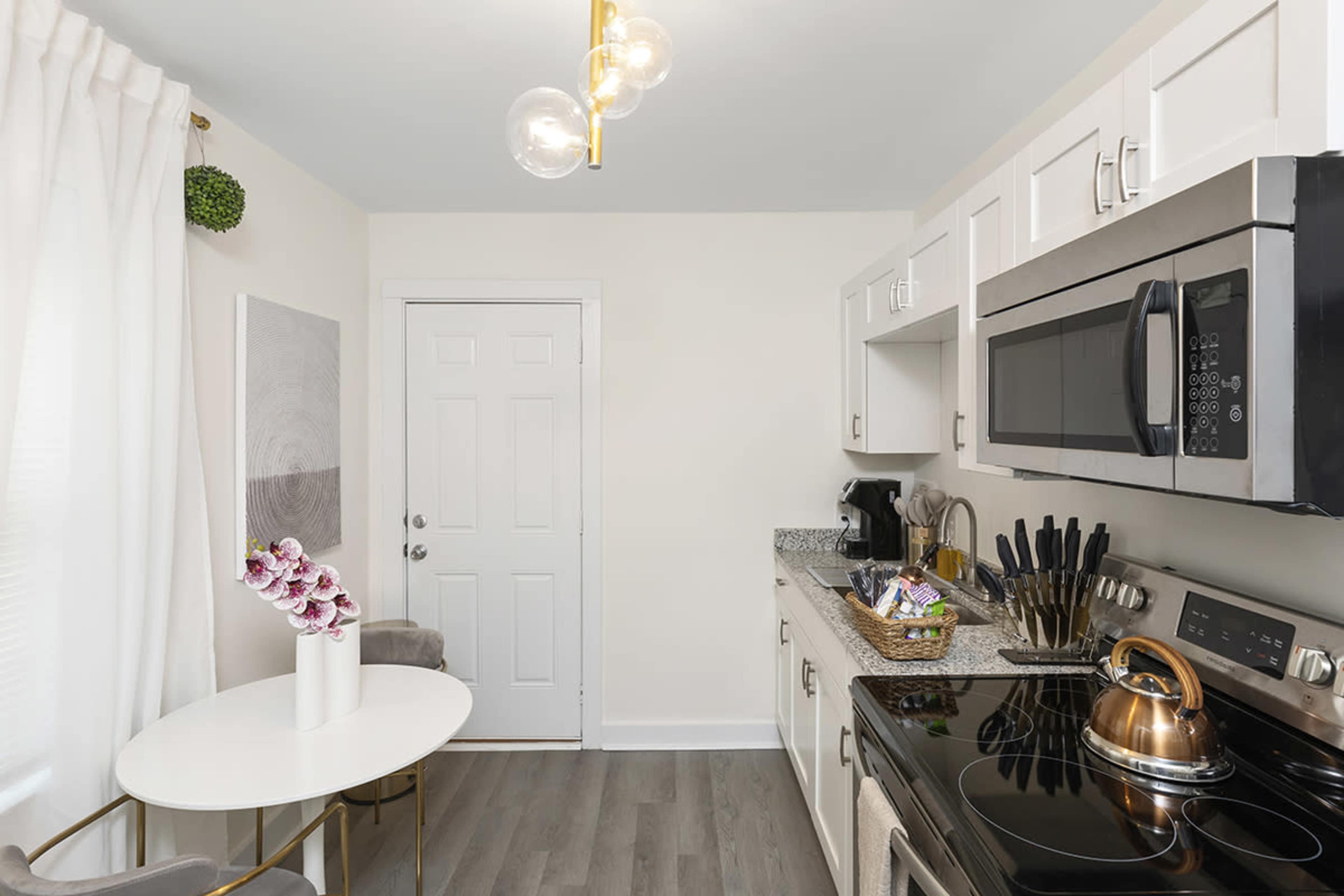 A modern kitchen with white cabinets, a black stove, a microwave, and a small round dining table with a vase of orchids.