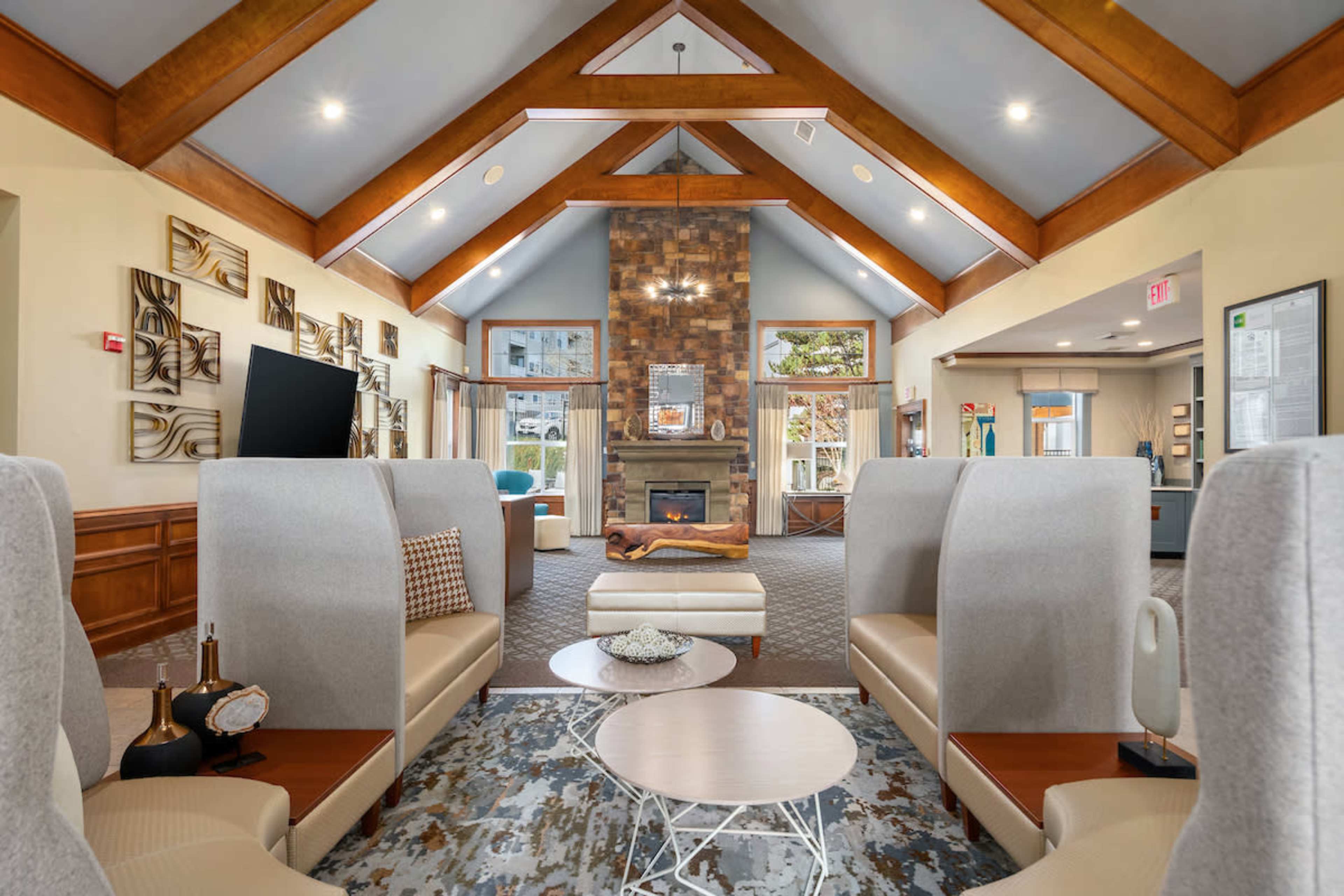 A modern lounge area featuring high wooden beams, a stone fireplace, and contemporary furniture arranged around a central coffee table.