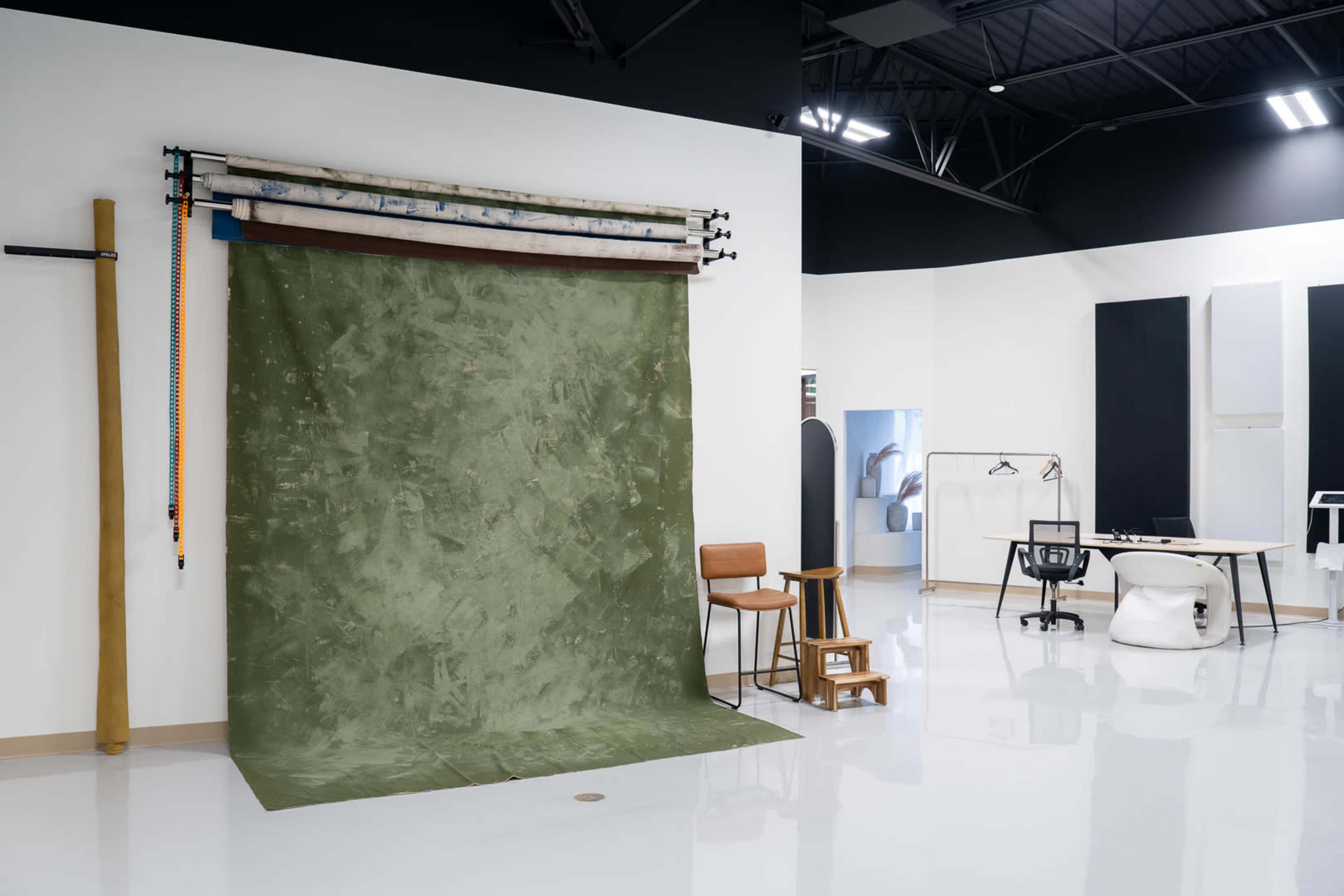 The image shows a photography studio featuring a green backdrop, chairs, and various equipment along the walls.