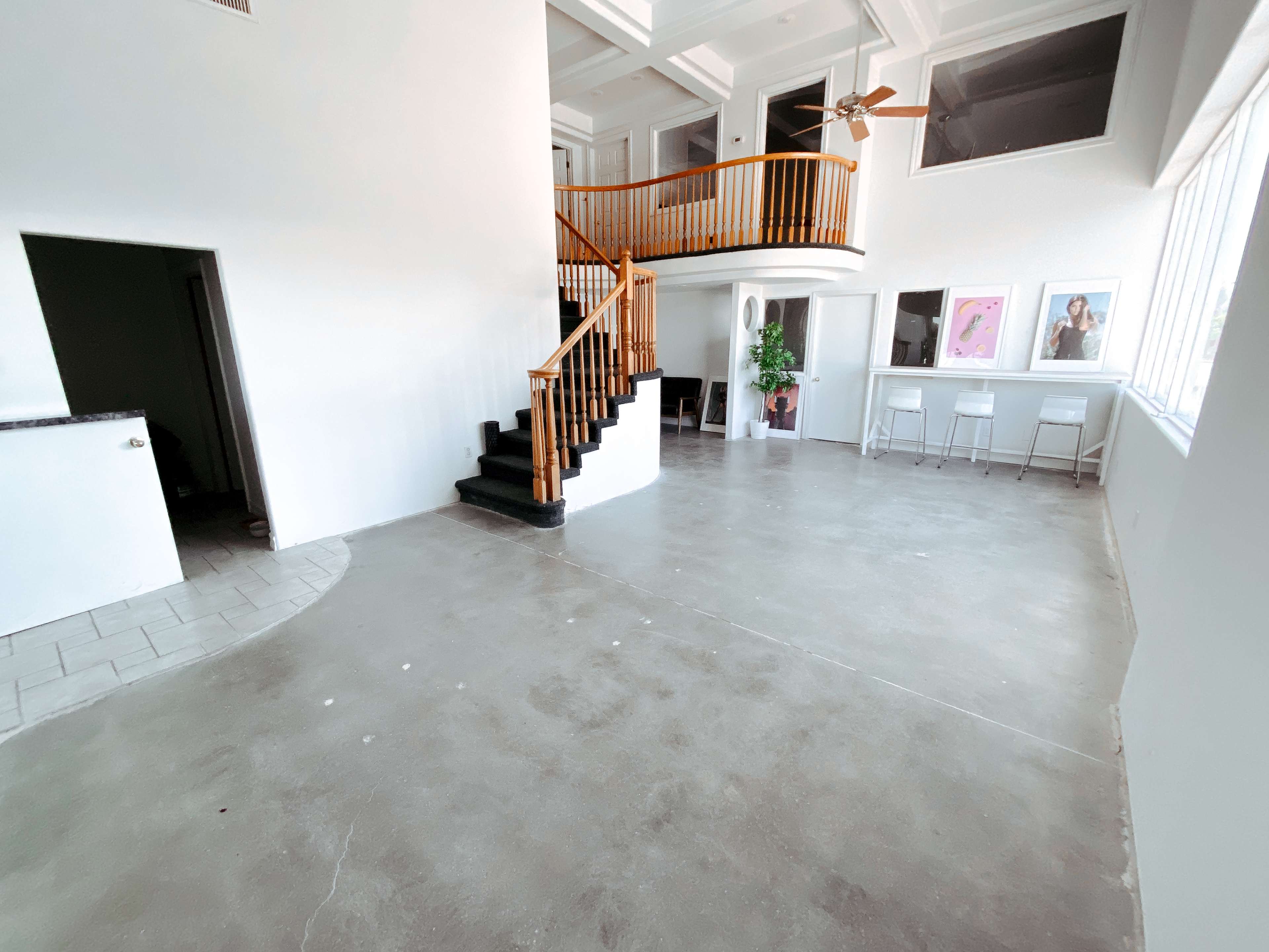 A spacious, open-concept living area featuring a staircase with wooden railing, large windows, and a minimalist design with a concrete floor.