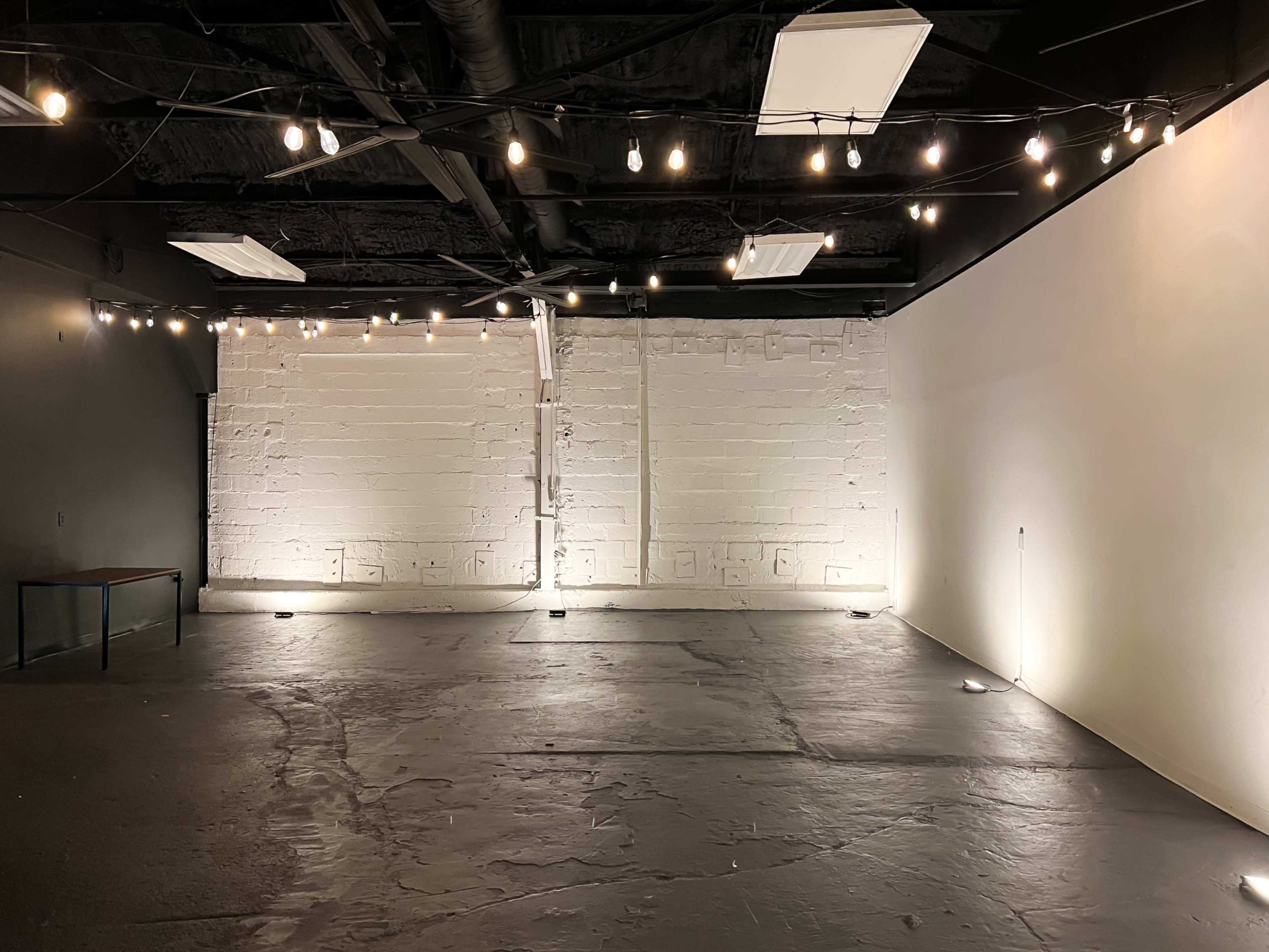 An empty room with exposed concrete floors, a white brick wall, and string lights illuminating the space.