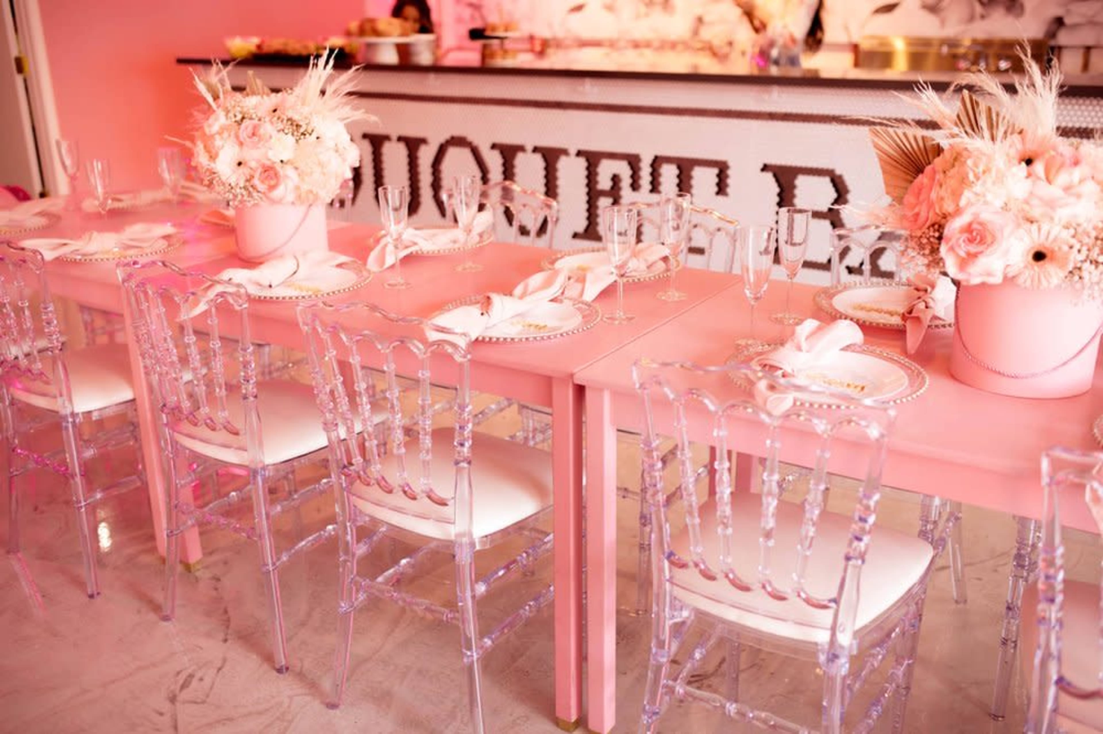 A pink-themed dining area features tables set with floral centerpieces and translucent chairs.