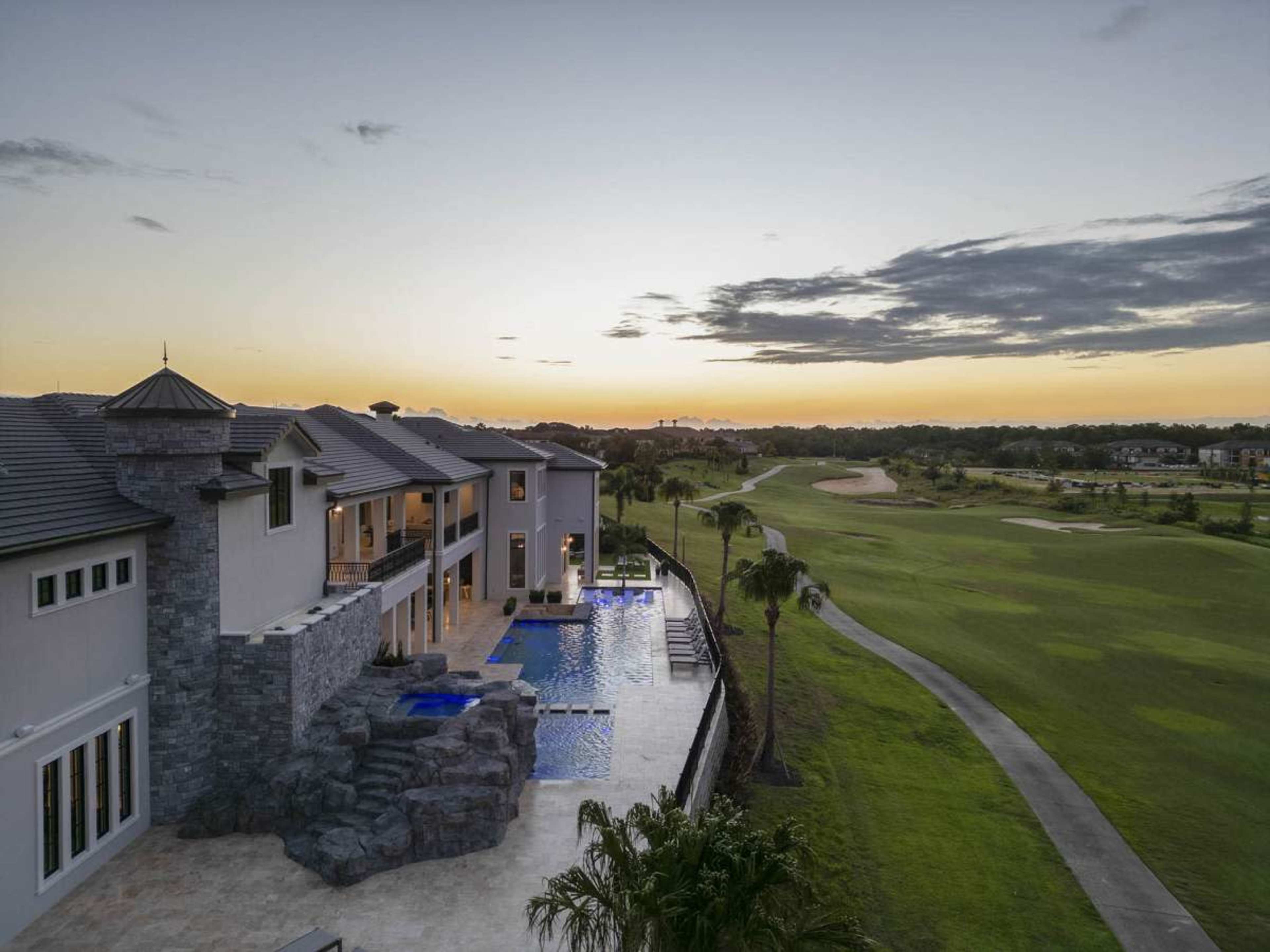 A luxurious modern house with a pool overlooks a golf course at sunset.