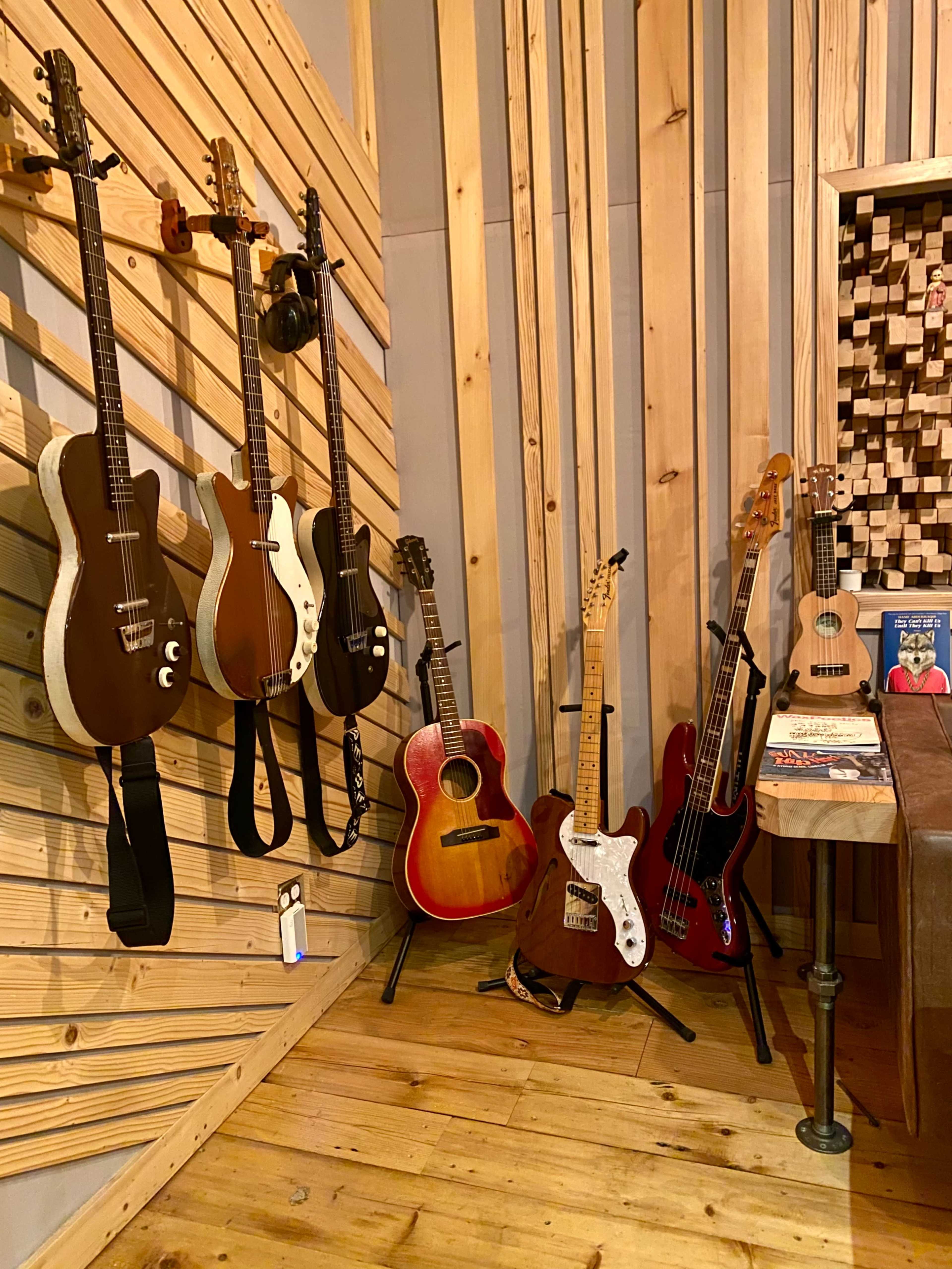 A collection of various guitars displayed against a wooden wall in a music studio.