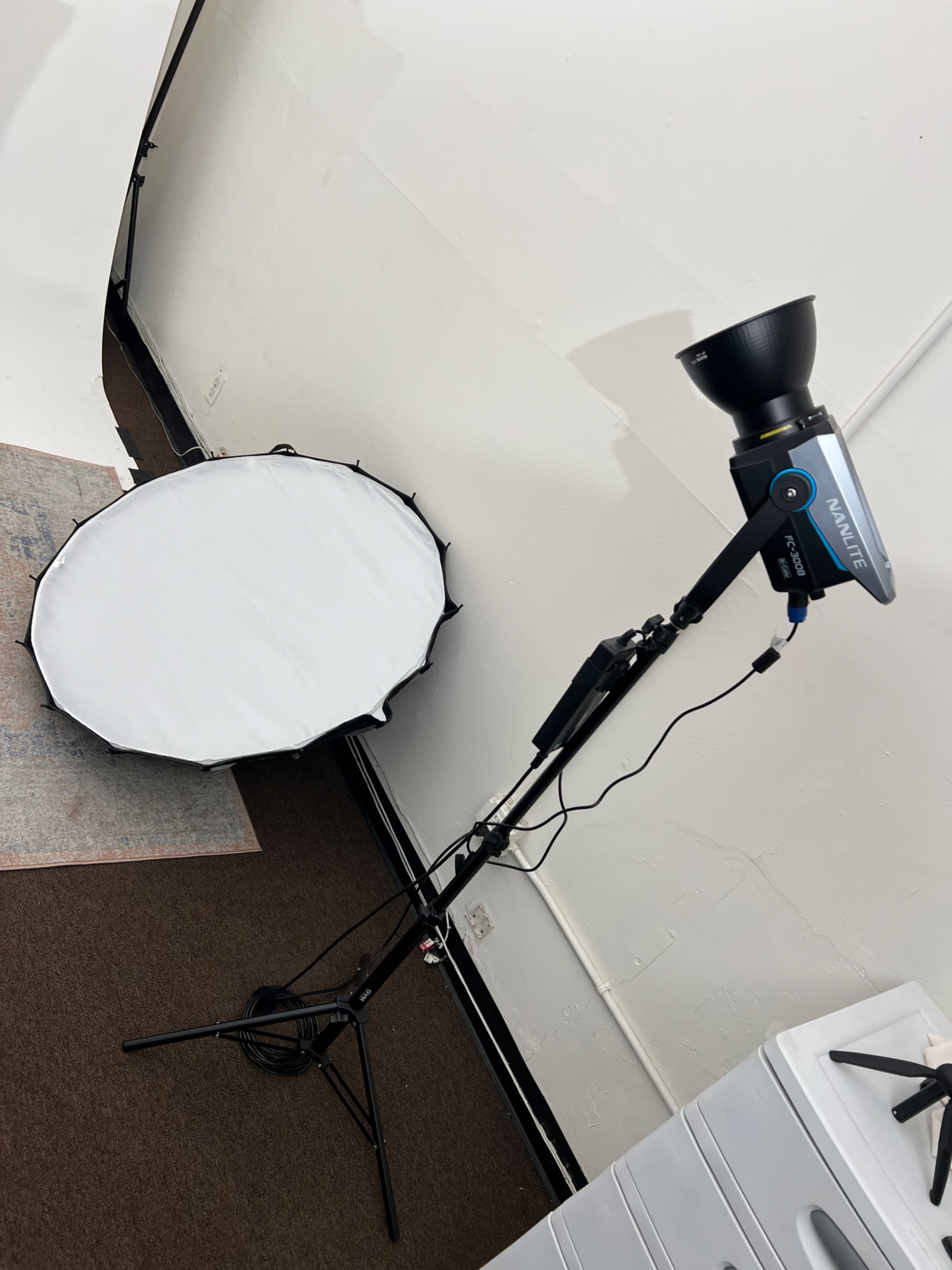 The image shows a photography setup with a light source mounted on a stand next to a large circular softbox on the floor.