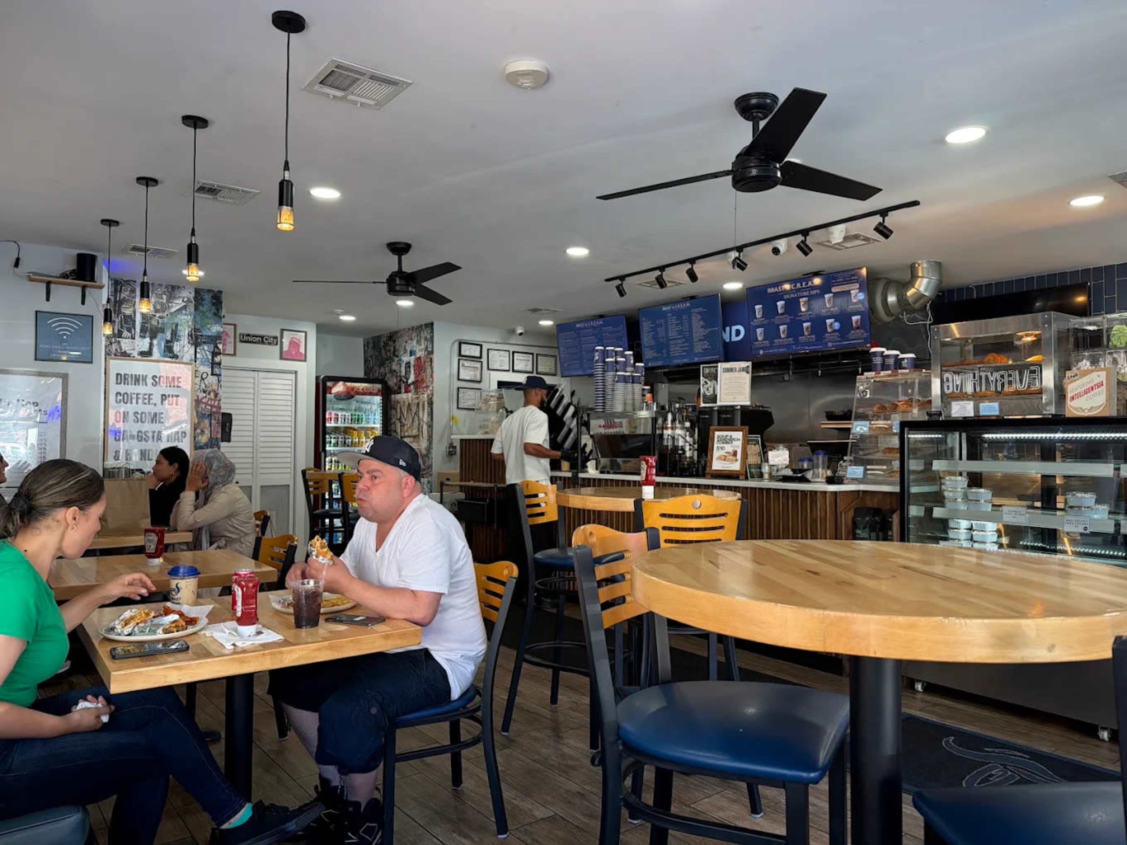 A bustling café features customers seated at wooden tables while a barista prepares drinks behind the counter.