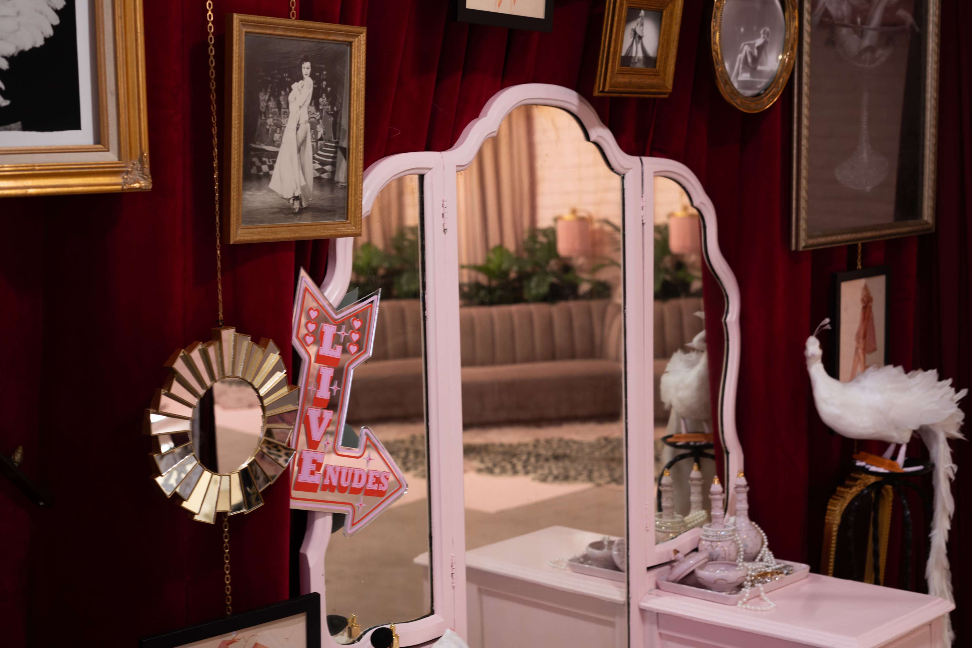 The image features a vintage vanity mirror surrounded by various framed photos and decorative items against a red velvet backdrop.
