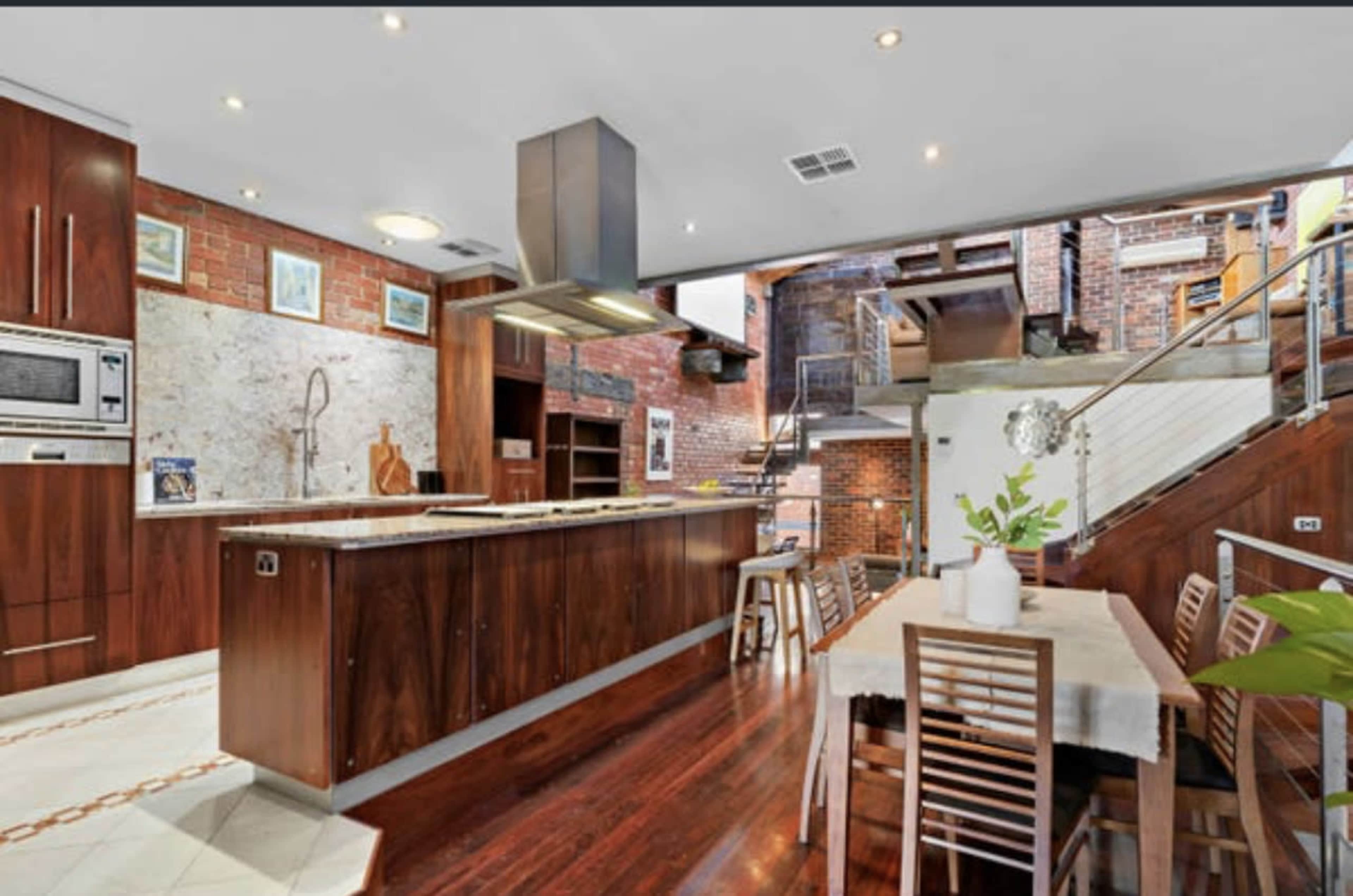 A modern kitchen featuring wooden cabinetry, a central island with a stovetop, and a dining area with a wooden table and chairs.