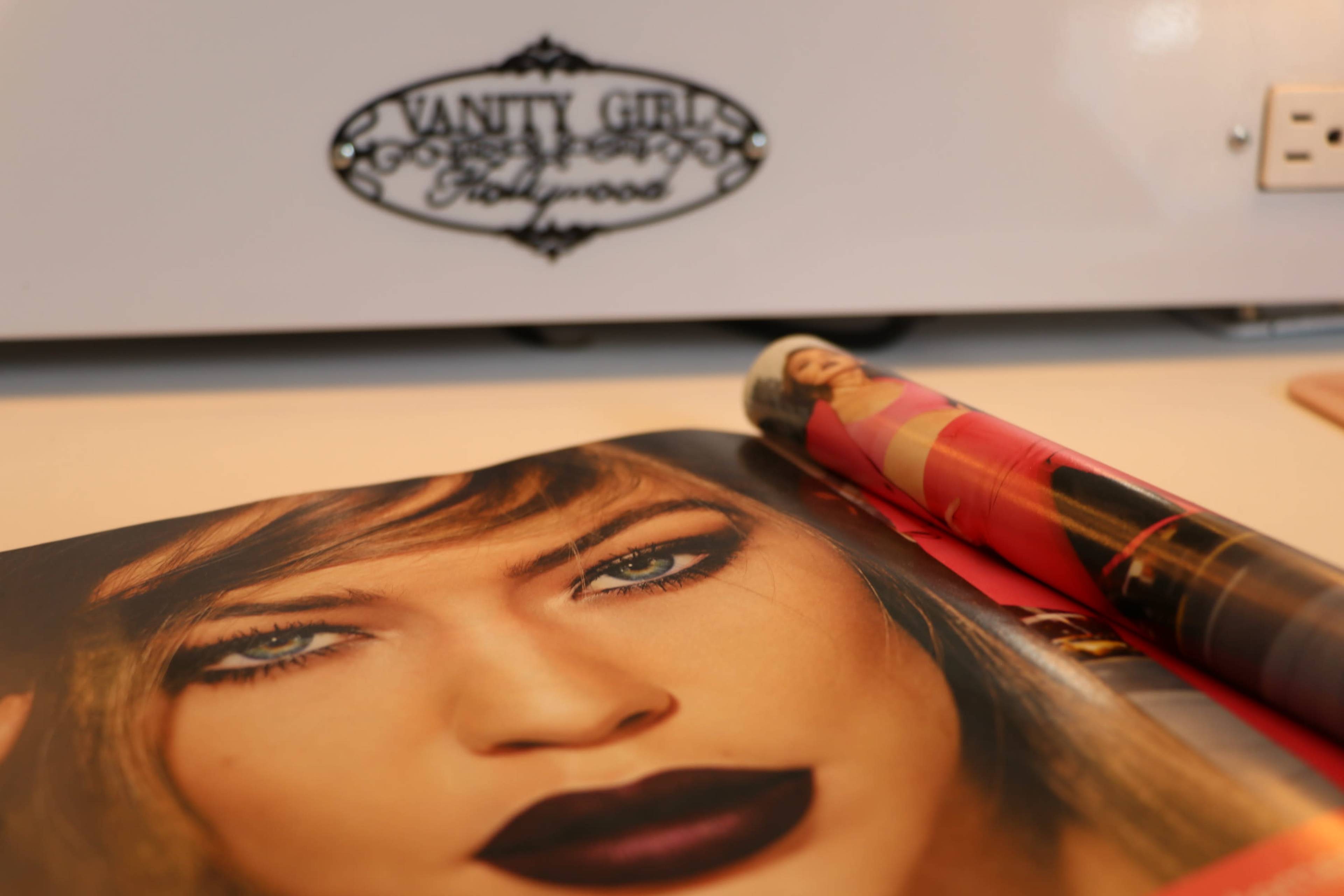 A magazine featuring a close-up of a woman's face with bold makeup lies on a table next to a rolled-up poster.