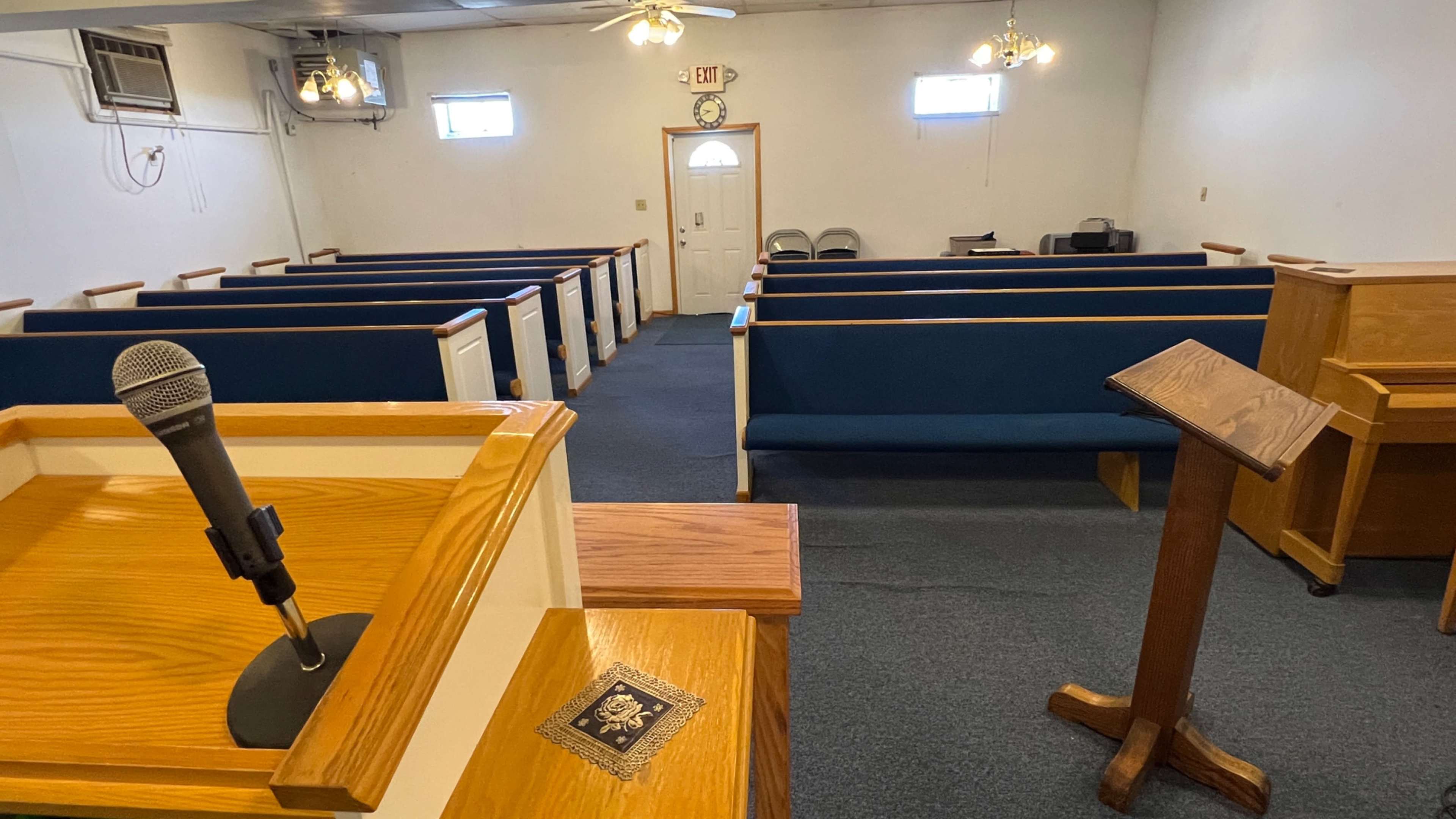 The interior of a small church with wooden pews arranged facing a podium and microphone at the front.