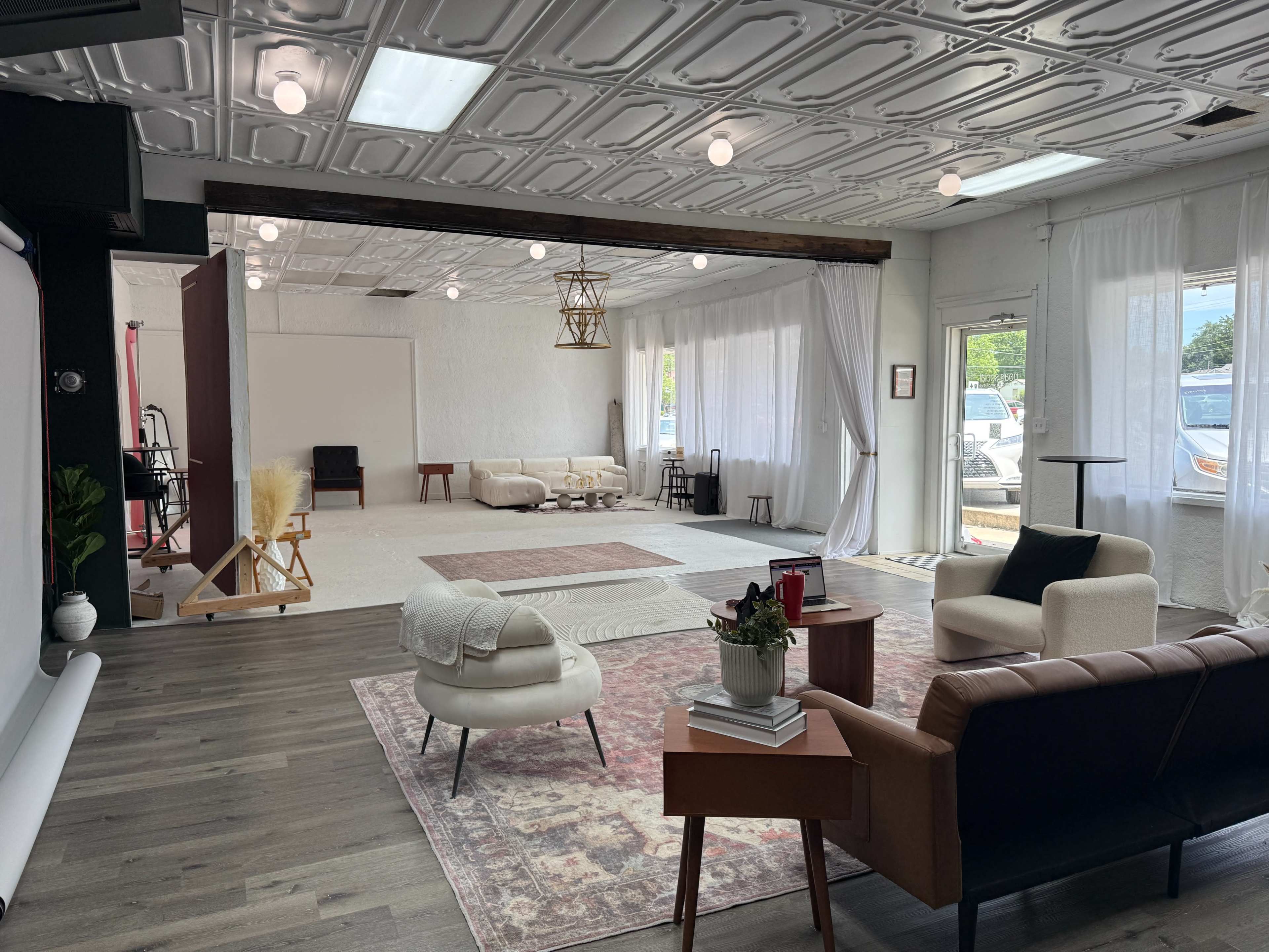 The image shows a spacious, well-lit studio with a combination of seating areas, a large open space, and decorative elements, including a rug and draped curtains.