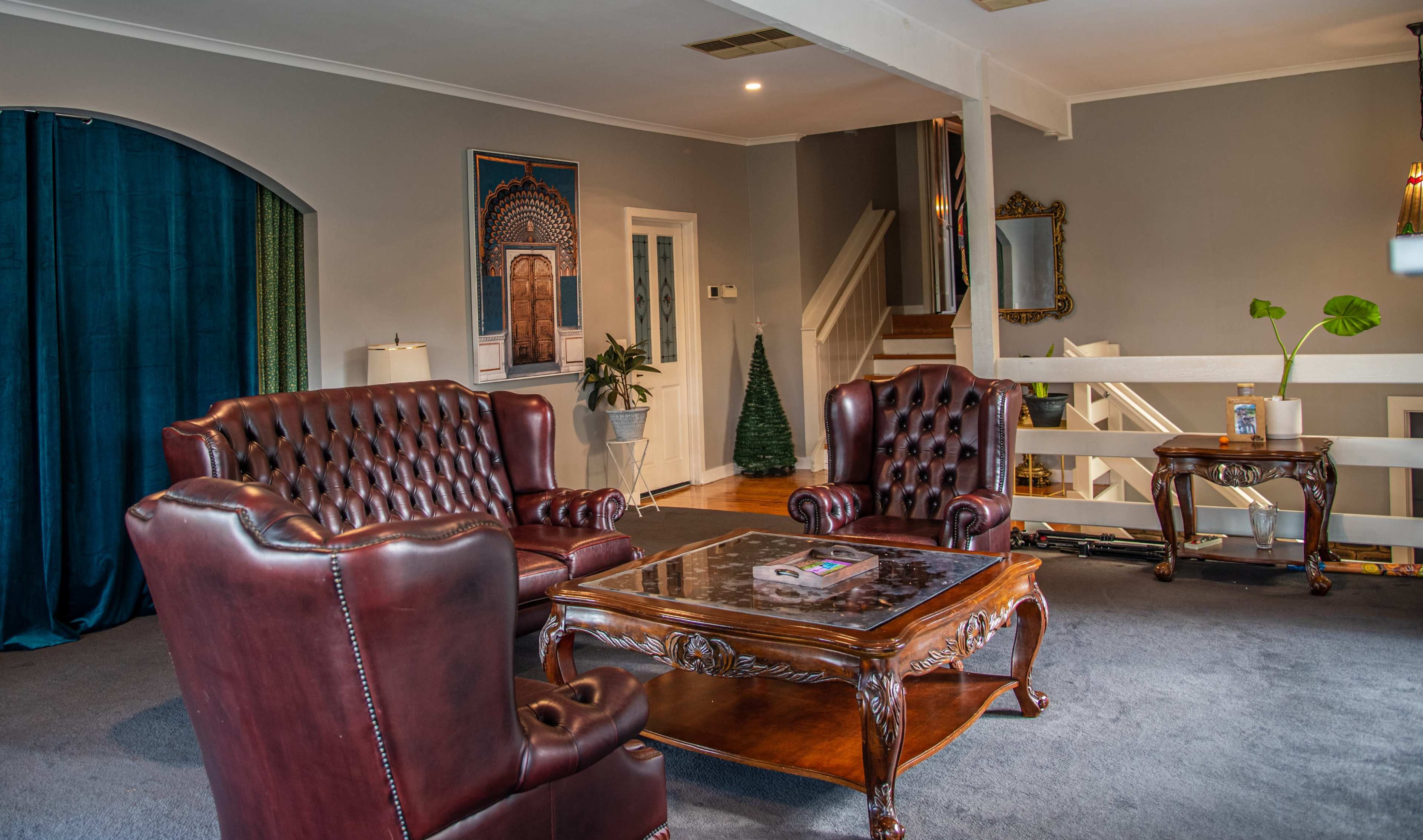 The image shows a living room with two leather armchairs facing a wooden coffee table, surrounded by gray walls and a staircase in the background.