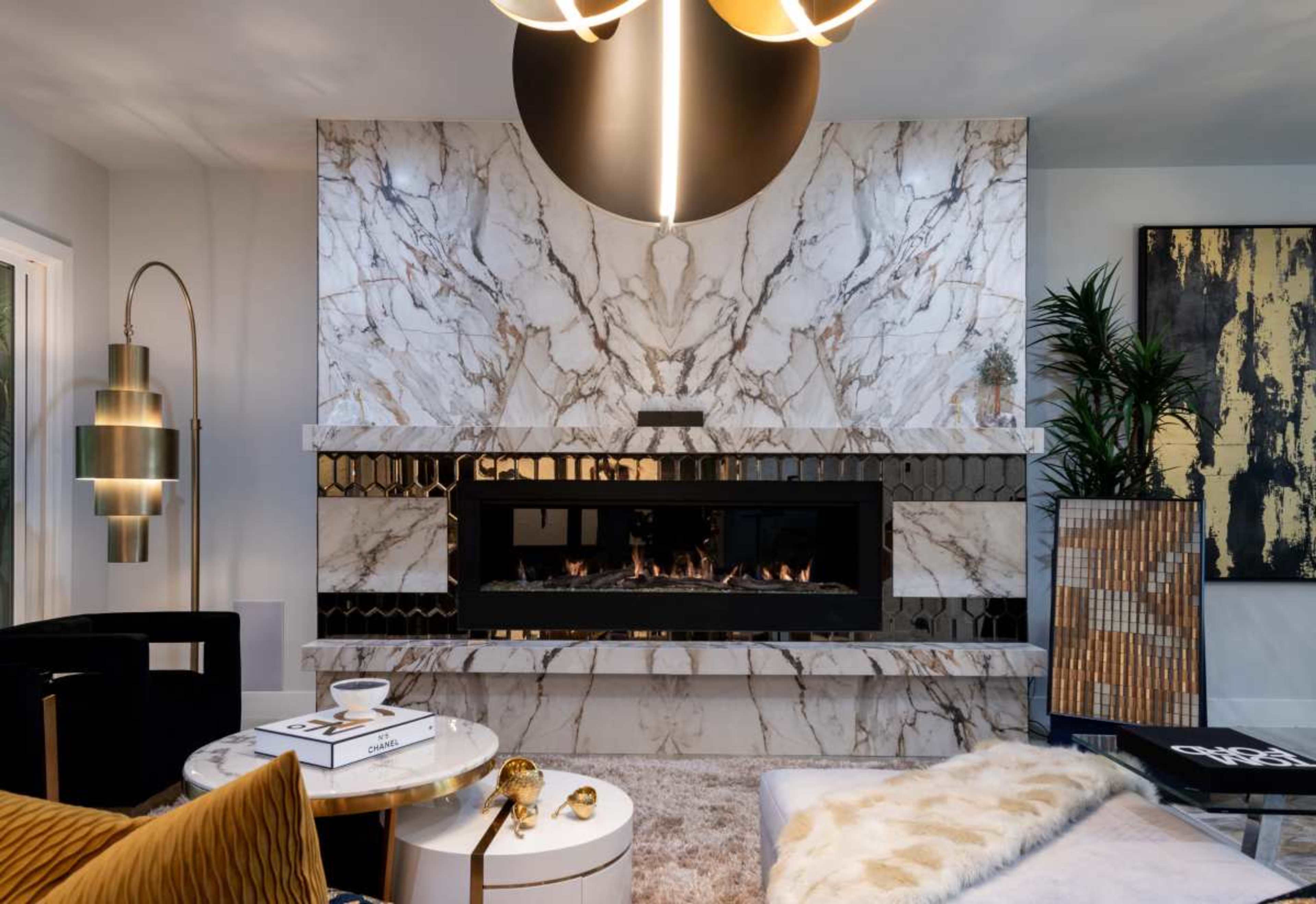 The image shows a modern living room centered around a sleek marble fireplace with a striking wall design, complemented by contemporary furniture and decorative elements.
