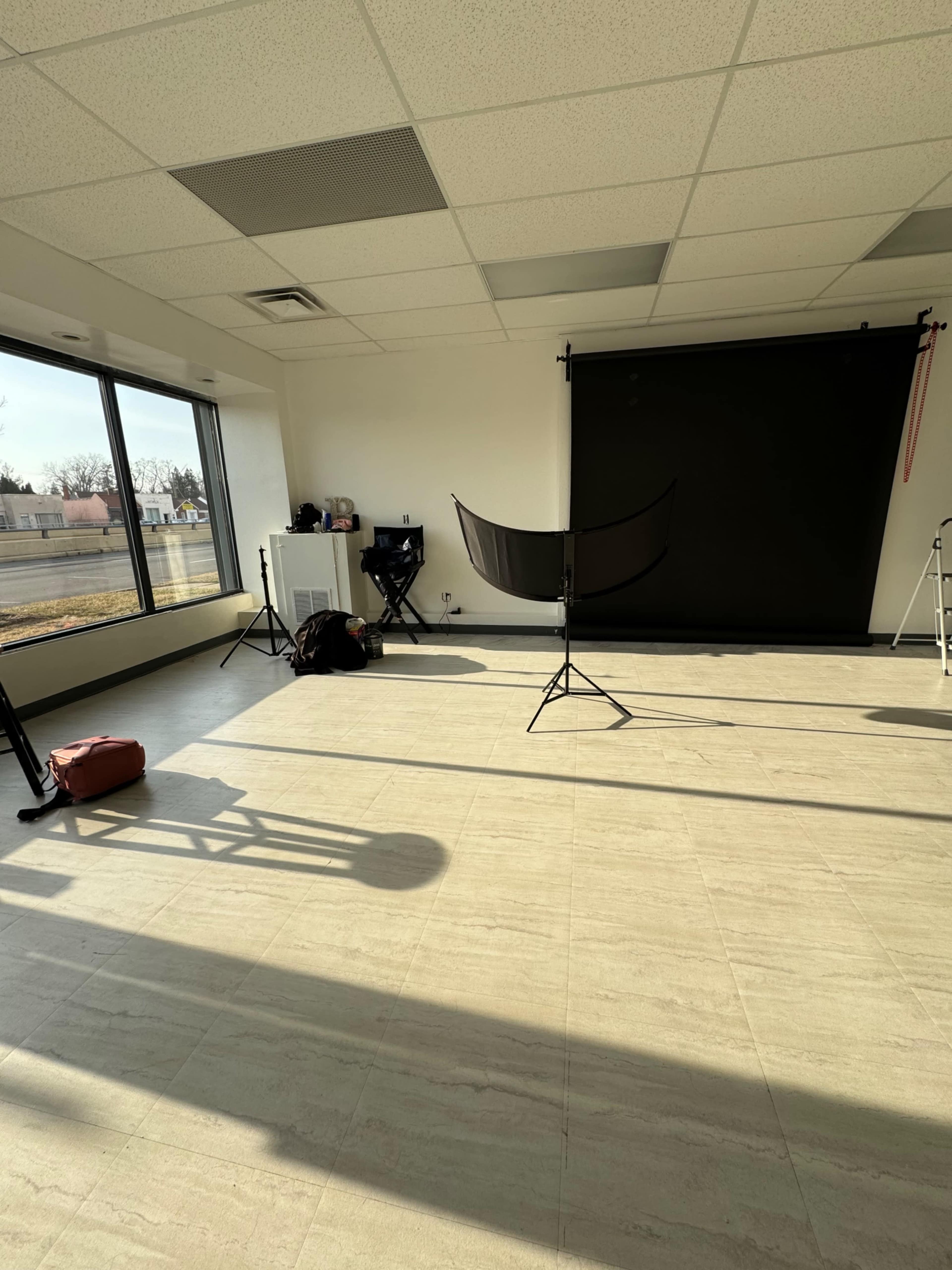 A photography studio with a black backdrop, lighting equipment, and a large window allowing natural light.