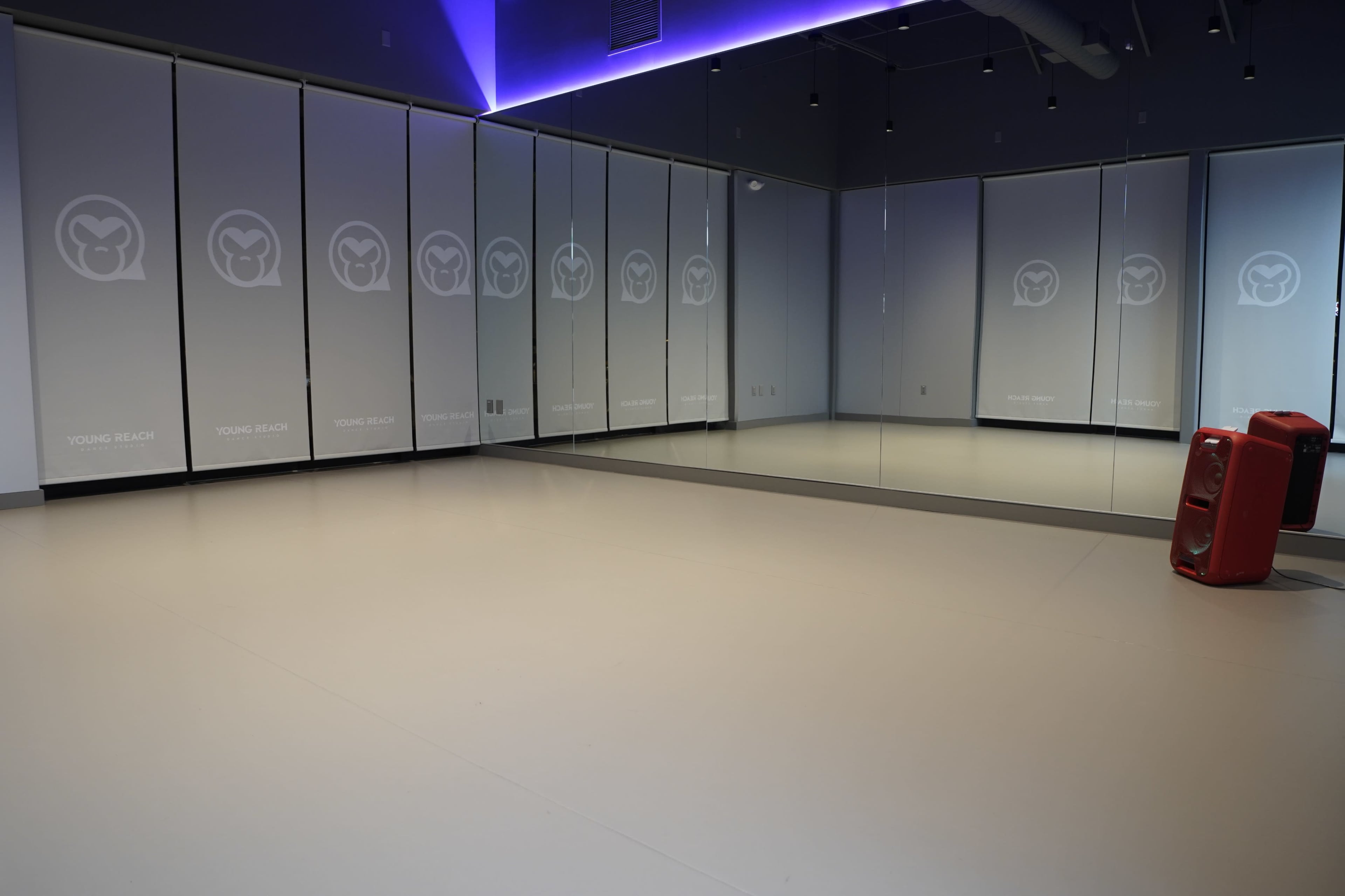 The image shows a spacious studio with mirrored walls and a colorful light feature, along with a red speaker in one corner.