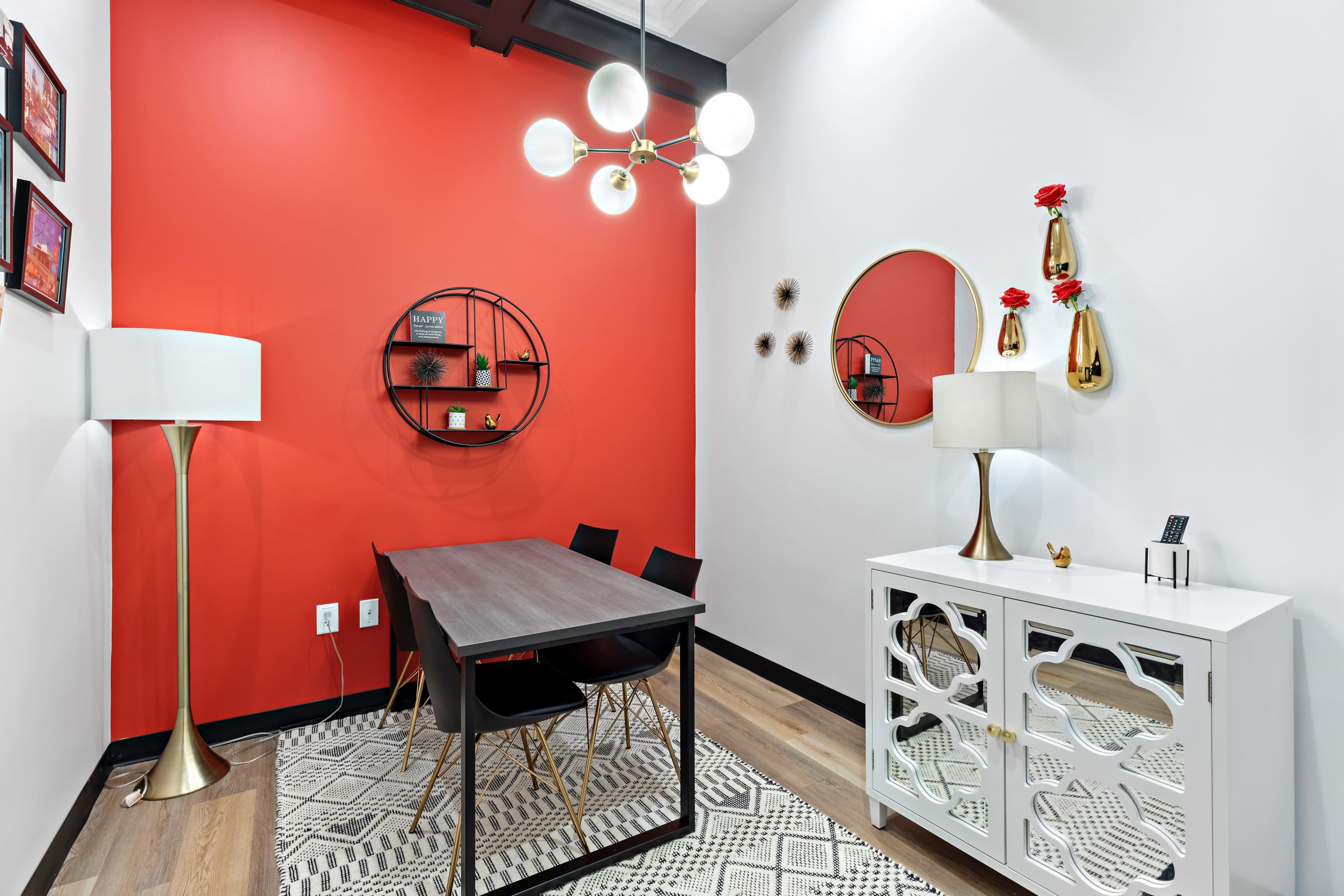 A modern dining area with a round table and four chairs, set against a red accent wall and featuring various decorative items.