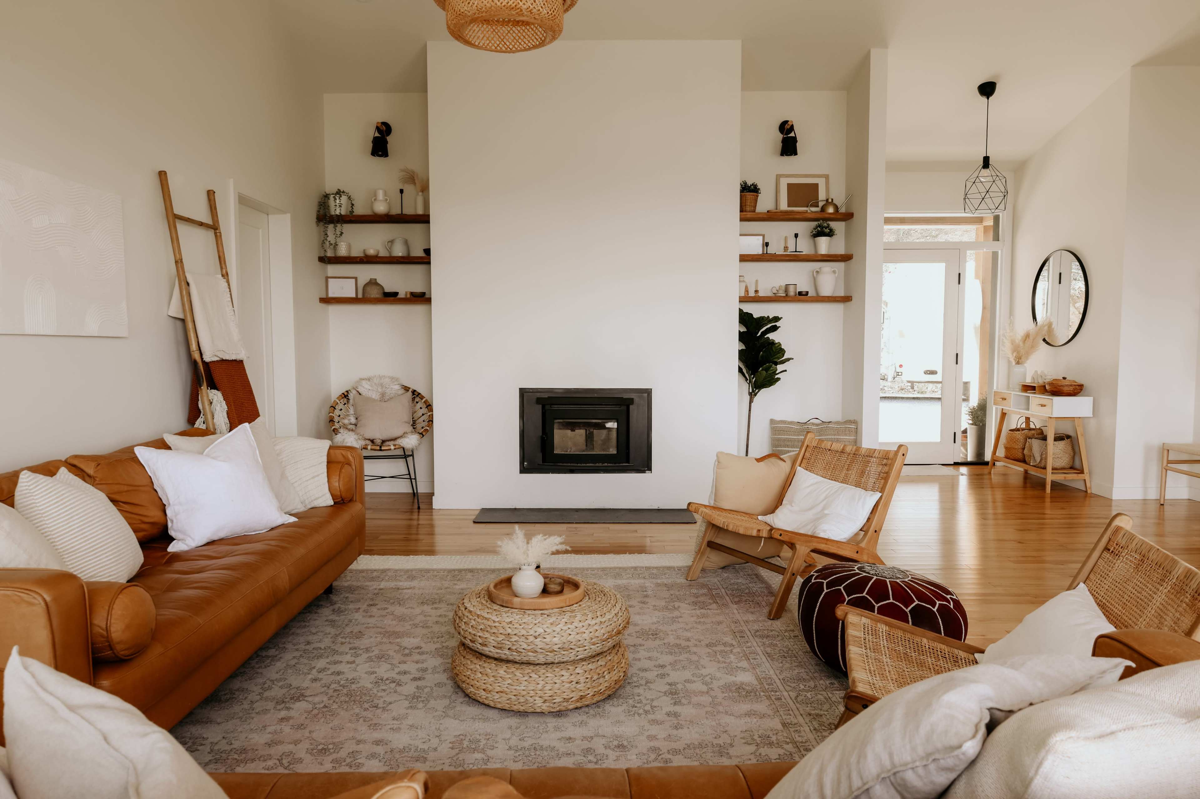 A cozy living room features brown leather sofas, a central woven rug, a modern fireplace, and shelves adorned with decorative items.