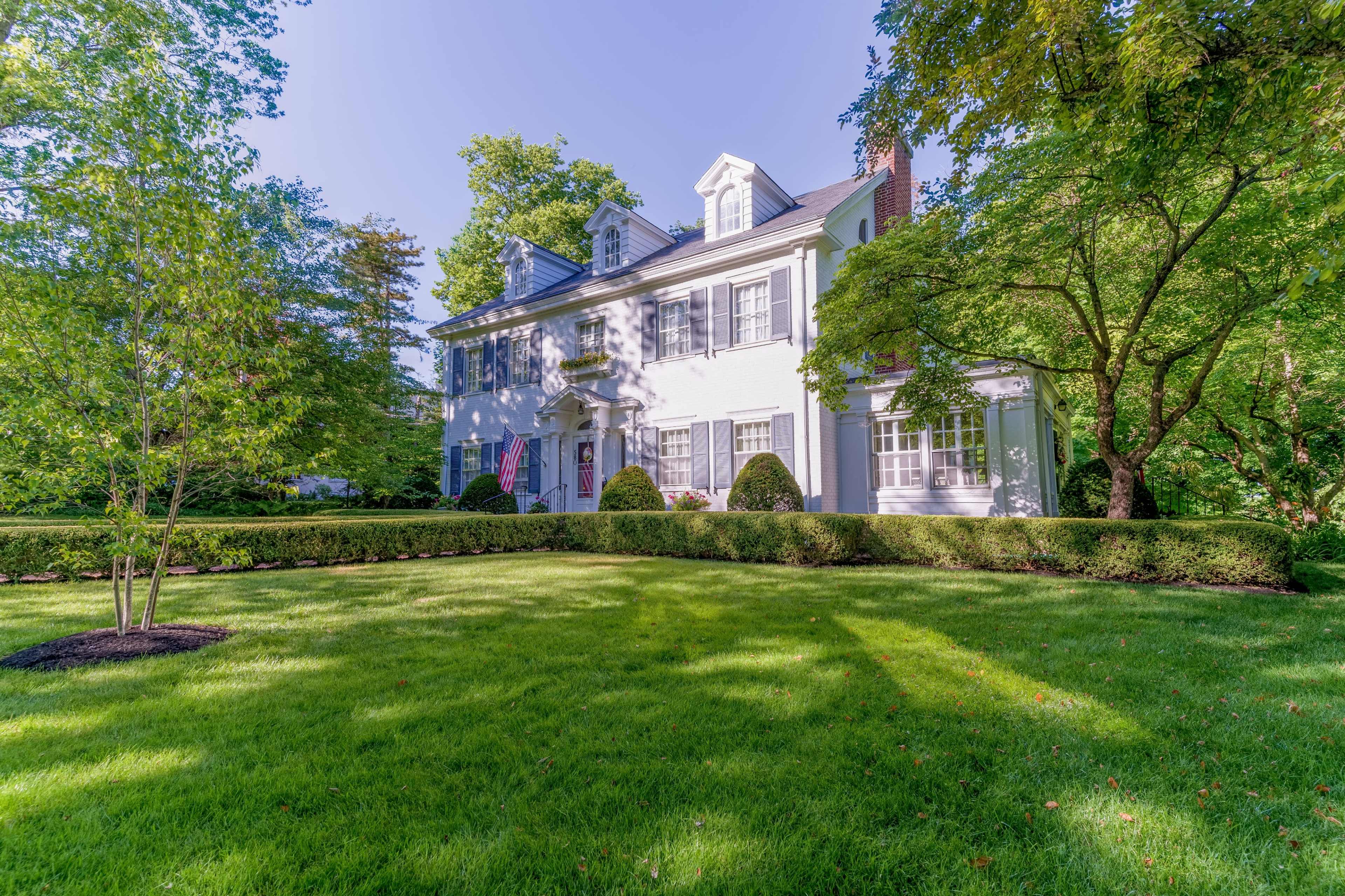 A white two-story house surrounded by well-maintained greenery and shrubs in a residential area.