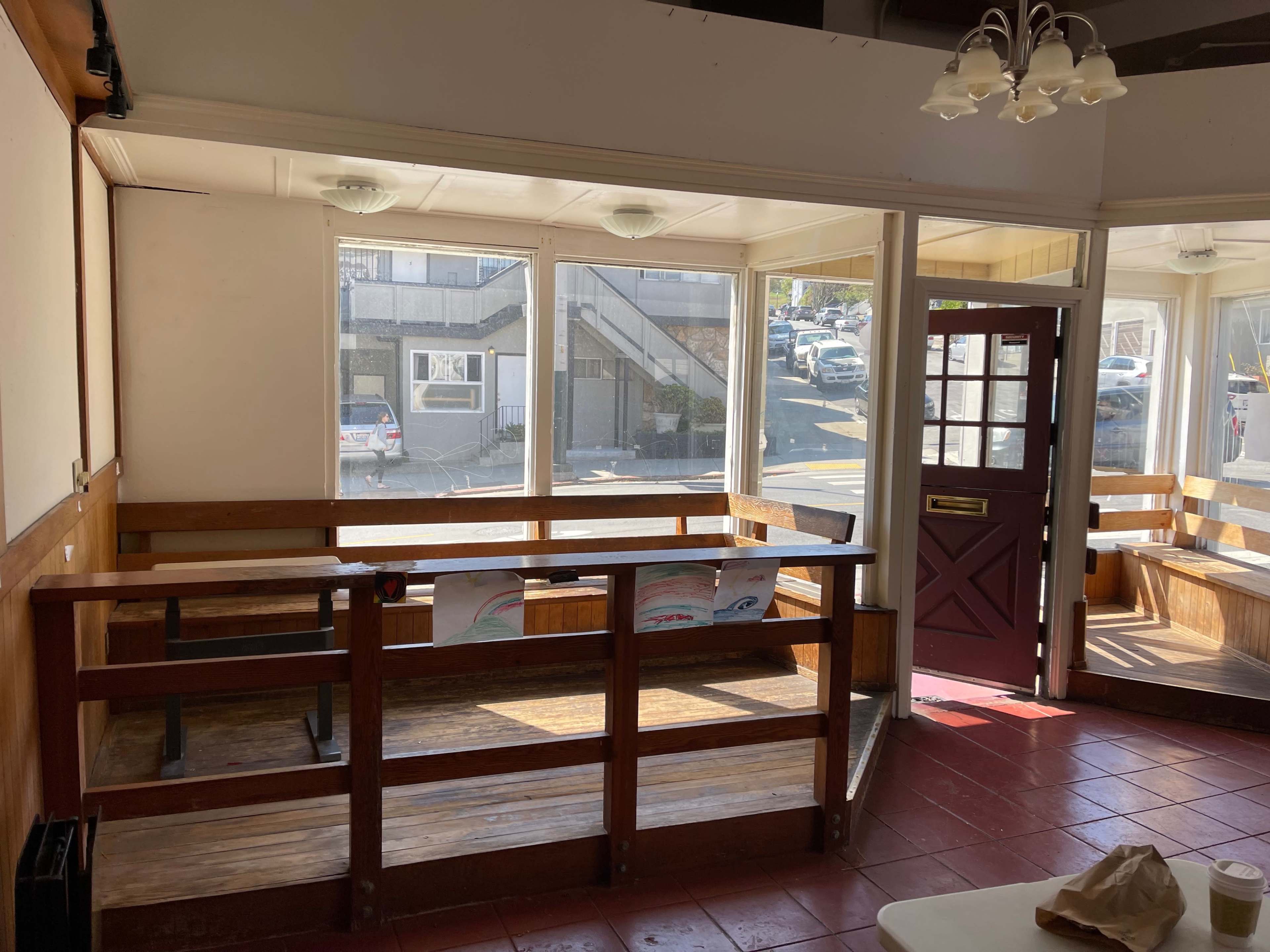 A vacant interior of a café or diner with wooden benches, large windows, and a red door.