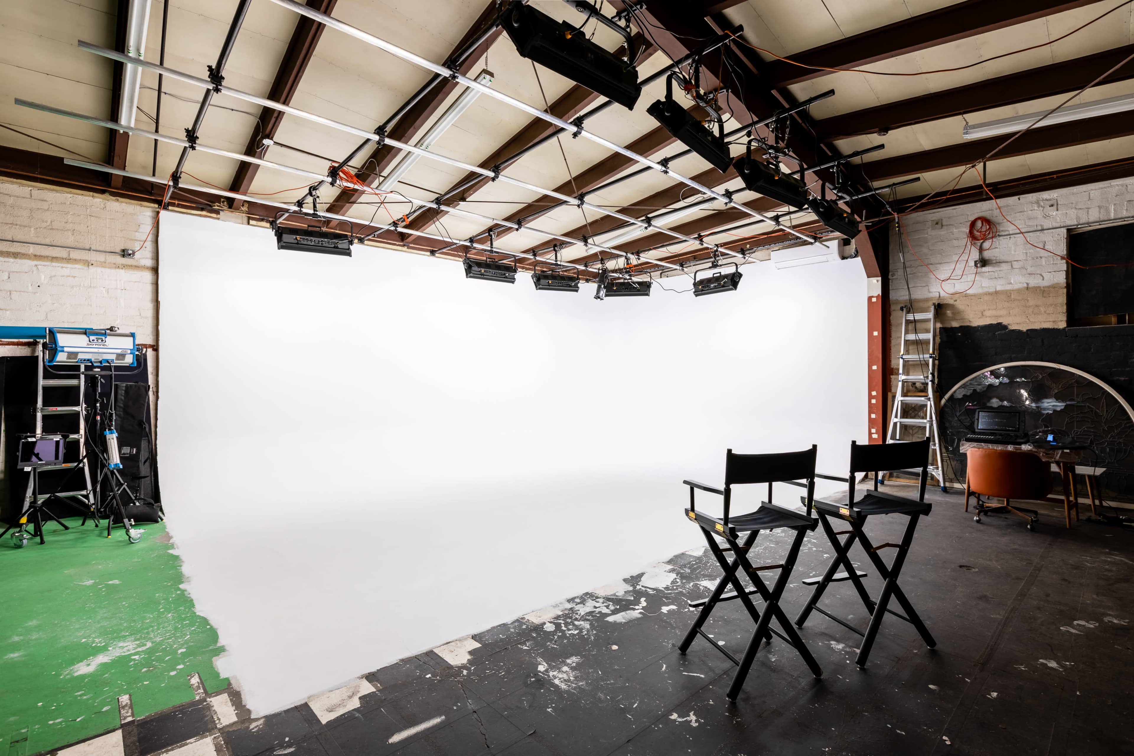 A spacious photography studio features a white backdrop, two director's chairs, and overhead lighting fixtures.