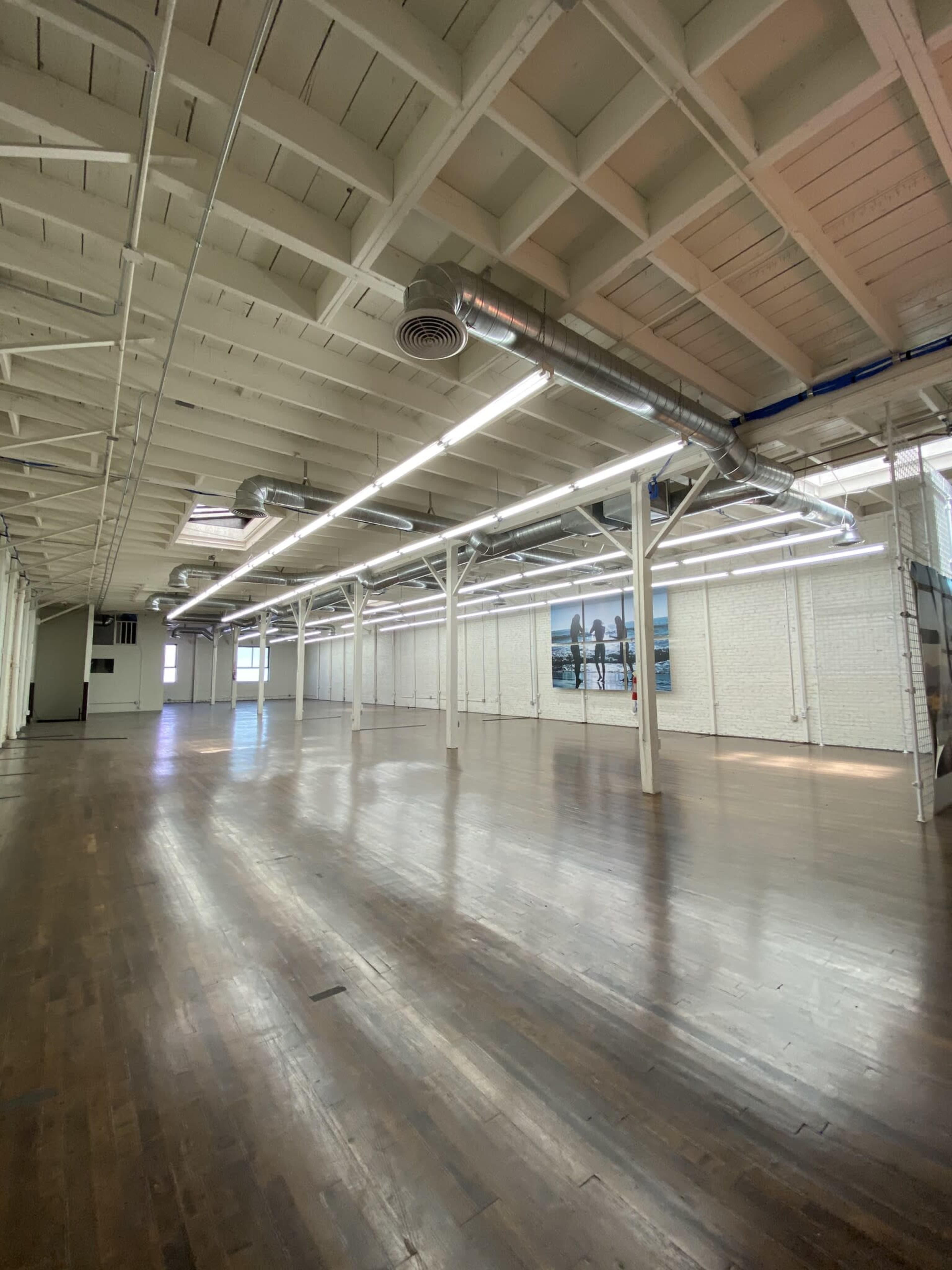 A spacious industrial-style room with wooden floors, high ceilings, and large windows.
