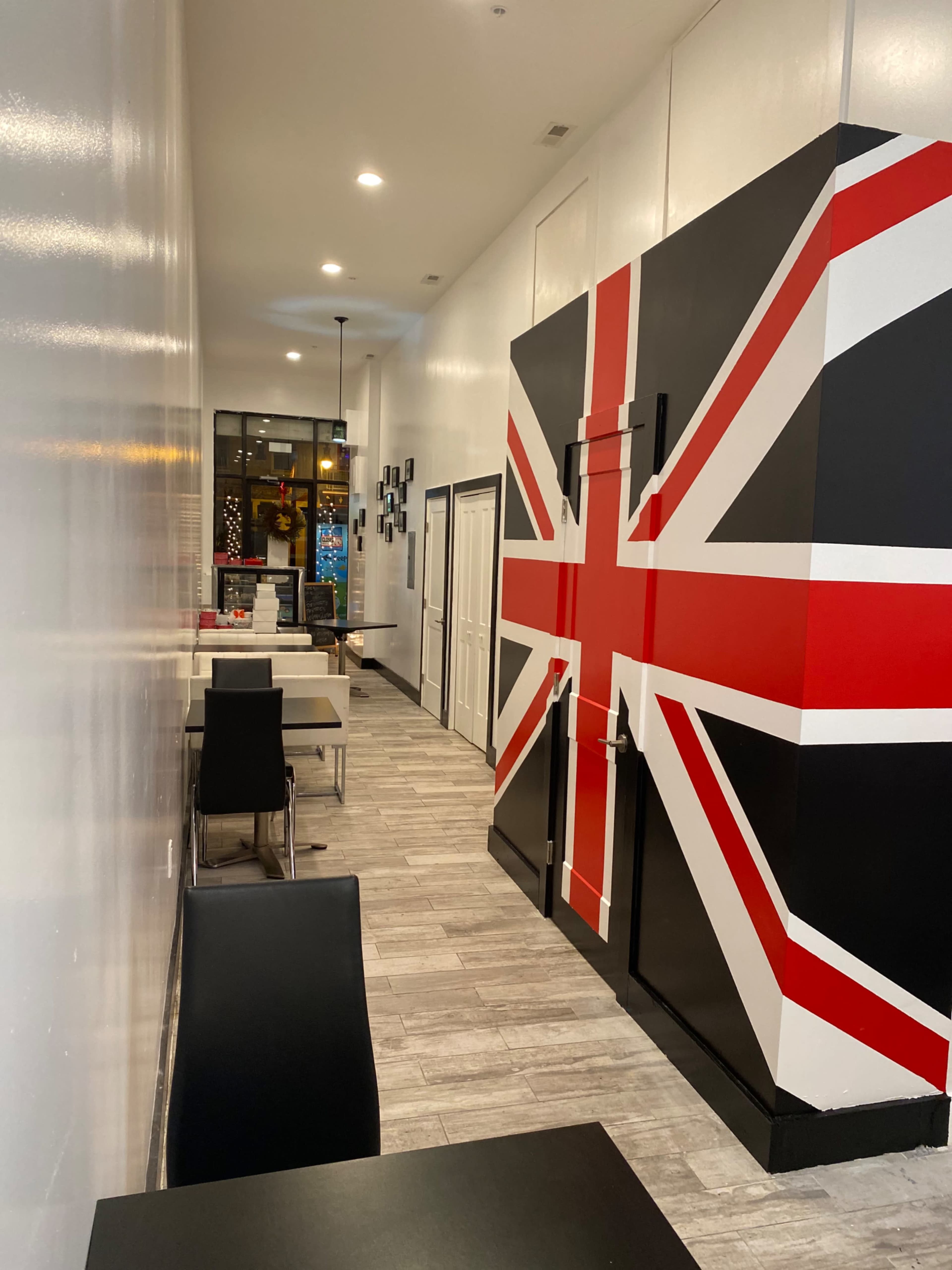 A narrow hallway in a restaurant featuring a large wall with a British flag design and several black chairs arranged around small tables.